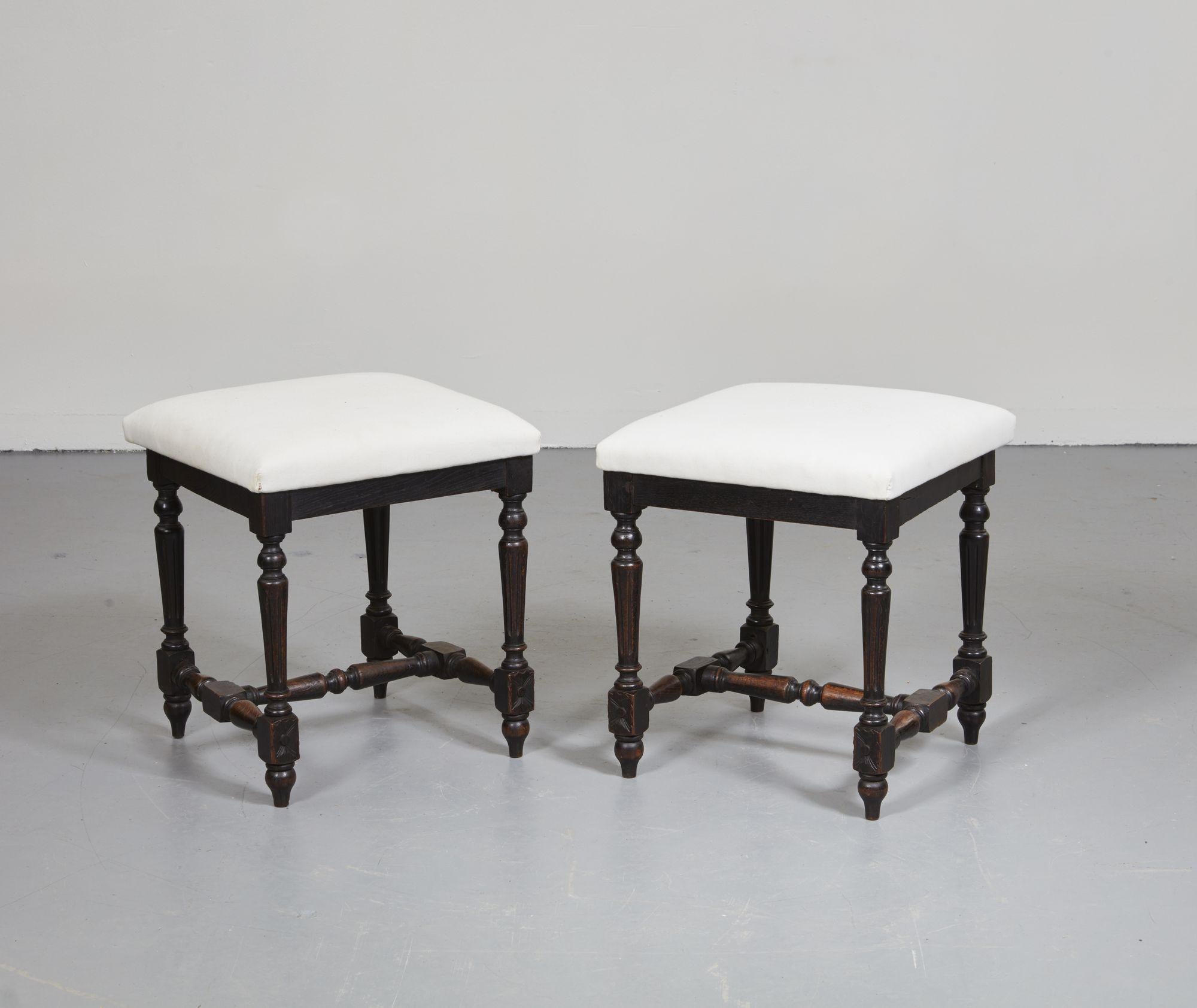 A pair of chair stools with upholstered white cotton tops over carved and turned stained beech legs joined by an H-stretcher. Adapted from a pair of early 20th century side chairs, with square tops added to trapezium bases. Useful, attractive,