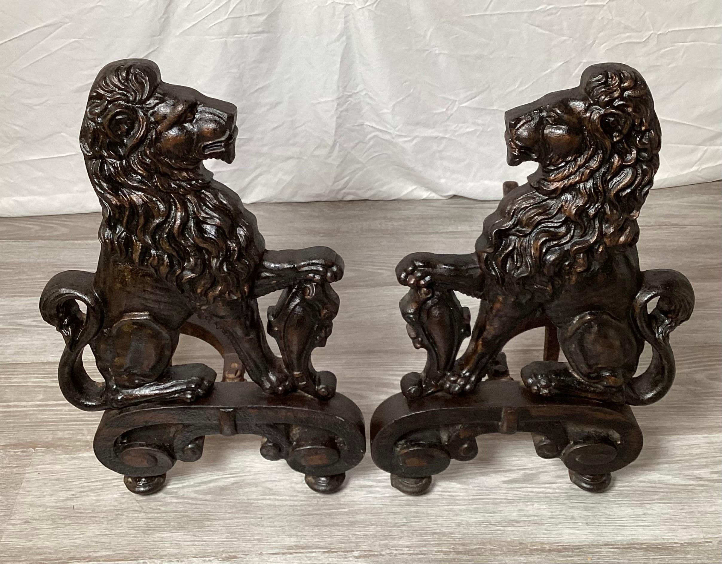 A Pair of blackened wrought iron lion motif andirons. The Tudor style of a profile of a lion with shield, being a mirror image of each other. 20.75 high.