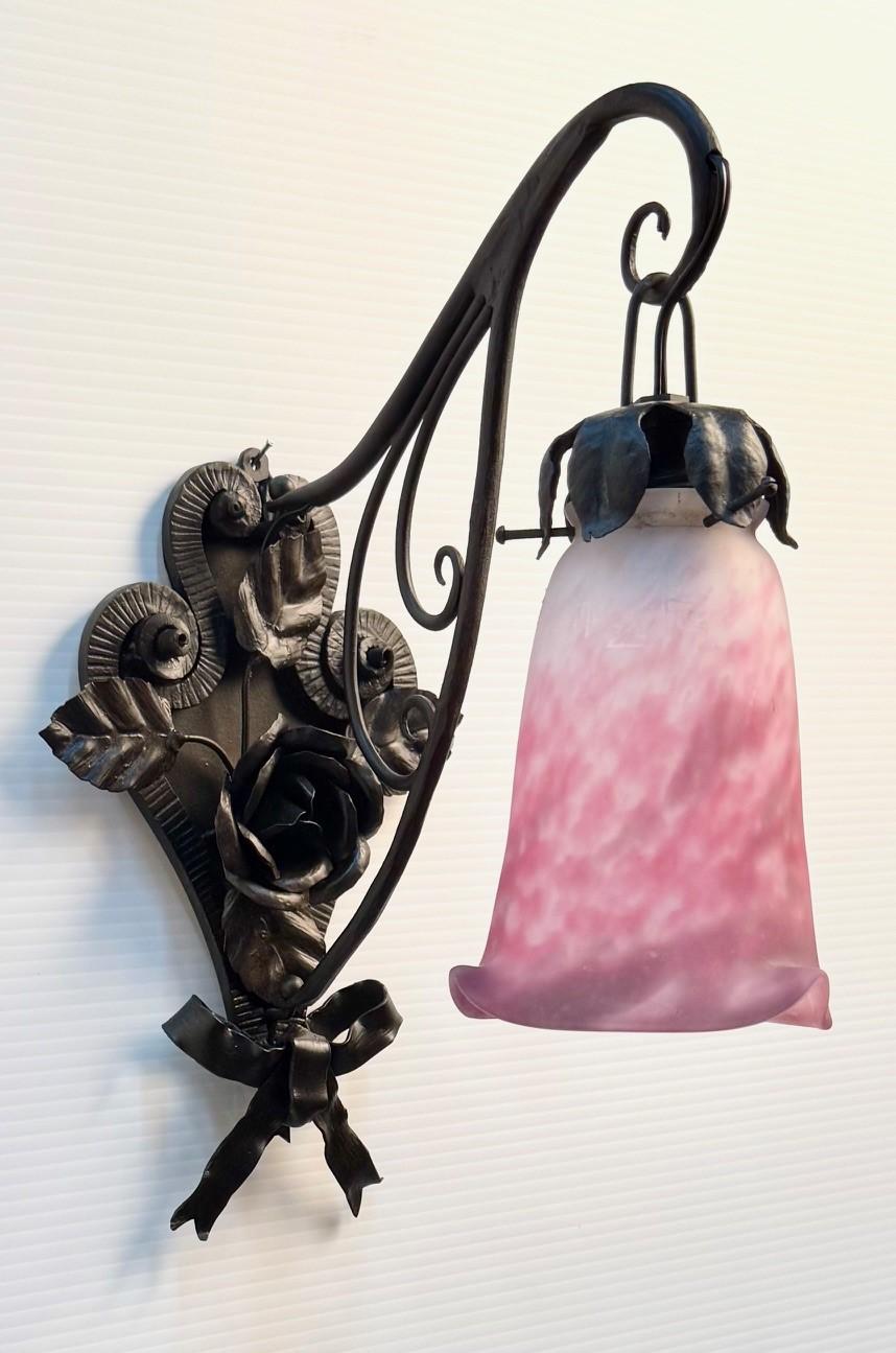 Cette paire est tout à fait dans l'esprit de l'Art déco et de cette période. Le cadre en fer est orné de feuilles, de têtes de fleurs et d'un nœud. Les abat-jours sont de Muller Frères, en framboise nuancée et en verre dépoli, avec un bord frangé.