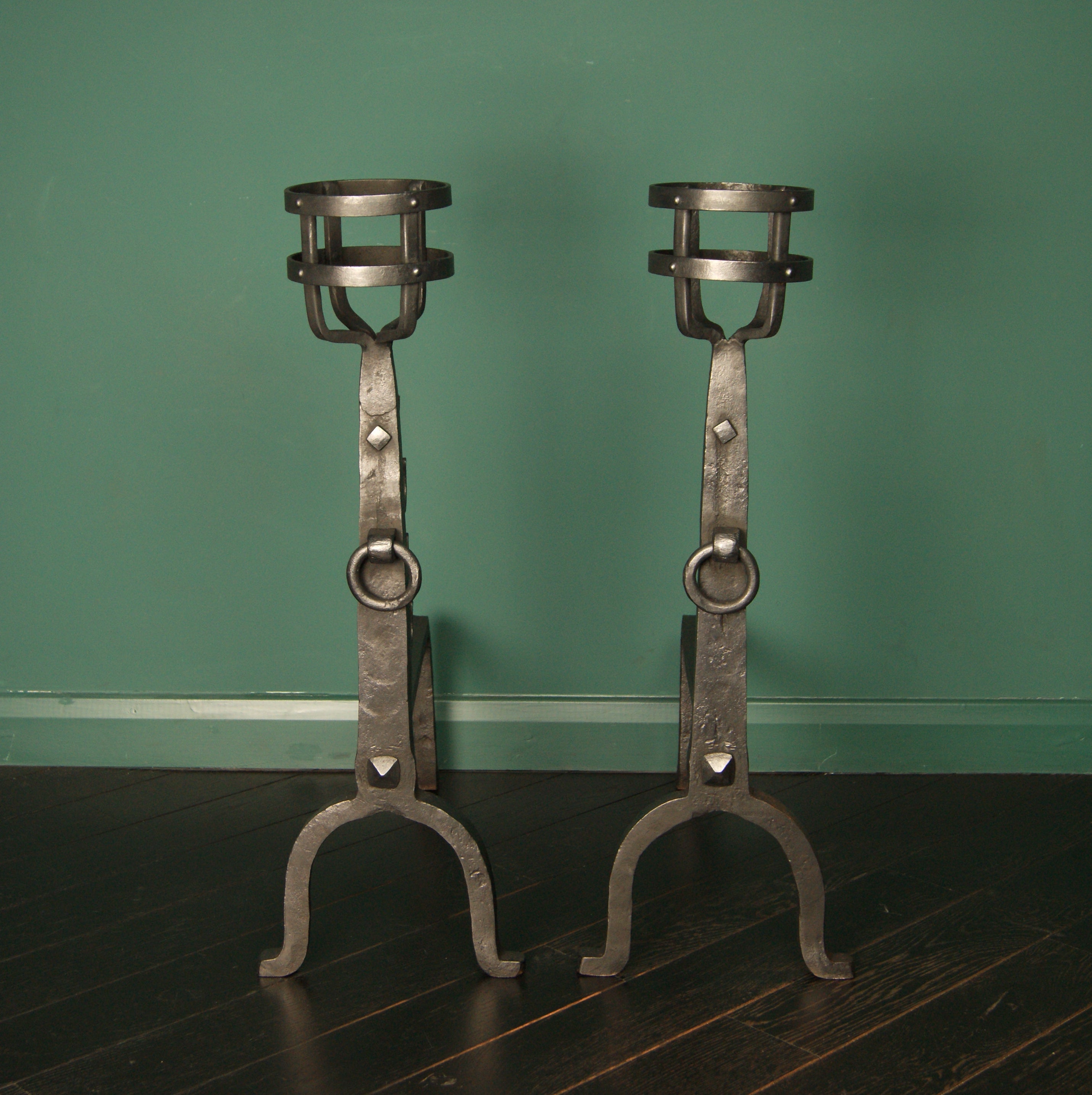 Ein Paar große, handgefertigte schmiedeeiserne Kresset-Kamin-Andirons mit vernieteten Korbblüten und Ringdetails an der Vorderseite der Ständer, die auf hohen Bogenstützen ruhen. Die Tiefe der Stammauflagen kann eingestellt werden. Ausgeführt in