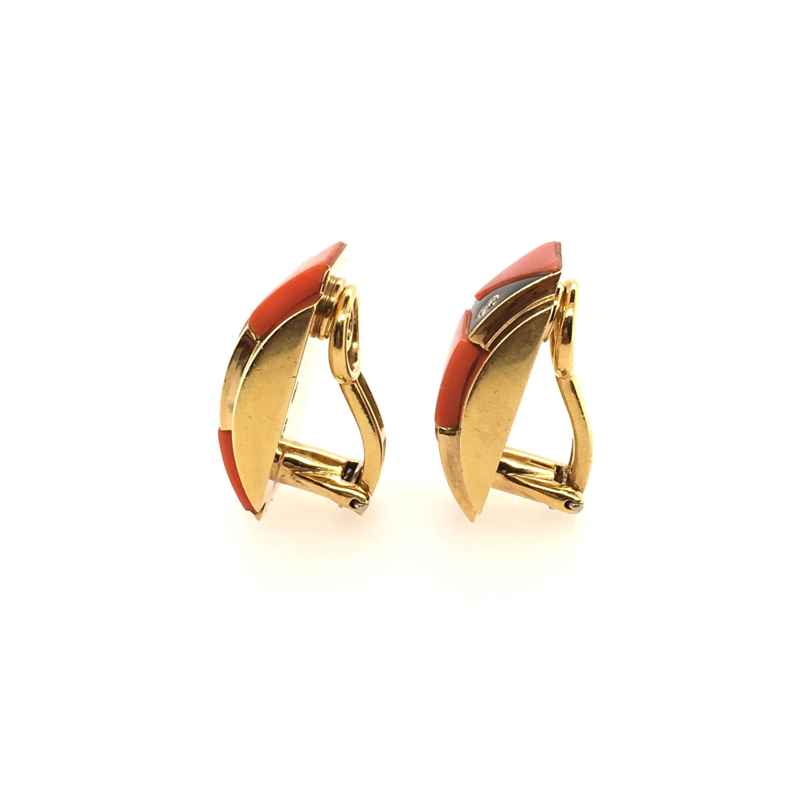 A pair of 18 karat yellow gold, coral, black onyx and diamond earrings.  Circa 1970. Italian. Designed as a polished gold half hoop, centering black onyx and coral geometric panels, enhanced by circular cut diamonds. Six (6) diamonds. Length is