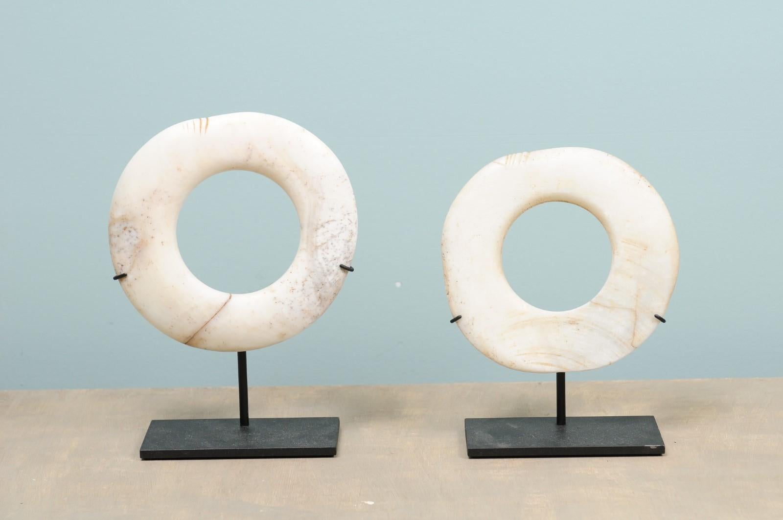 A pair of Yua Wenga currencies from the early 20th century on custom iron stands. These antique tribal currency pieces from Papua New Guinea have been carved from giant clam shells with pieces of bamboo. Yua means money and Wenga are clam rings. The
