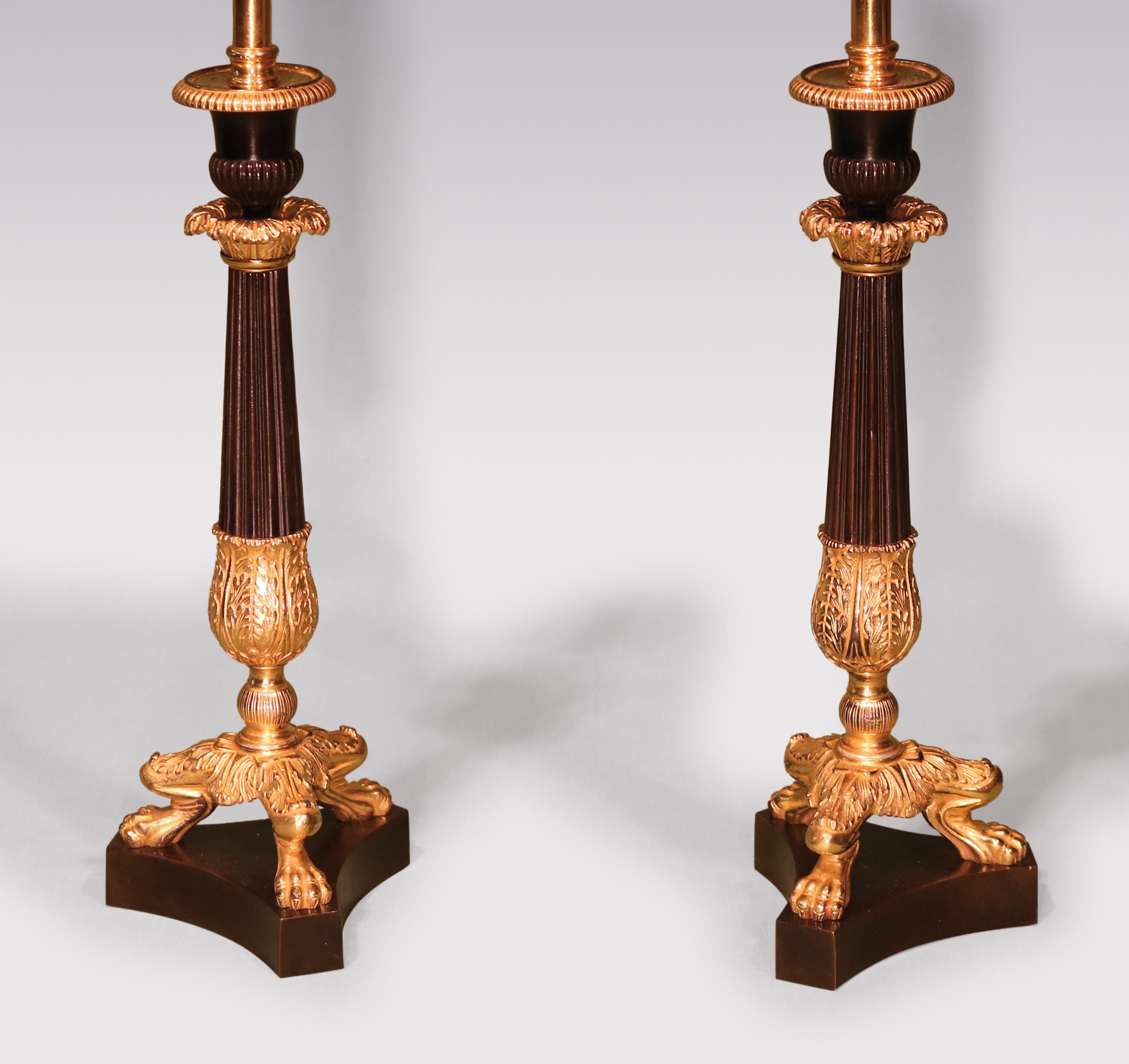 A pair of early 19th century bronze & ormolu fluted candlestick lamps having urn-shaped nozzles above reeded, tapering stems with acanthus leaf decoration, supported on well-cast lion’s paw feet ending on triform platform bases. Height of