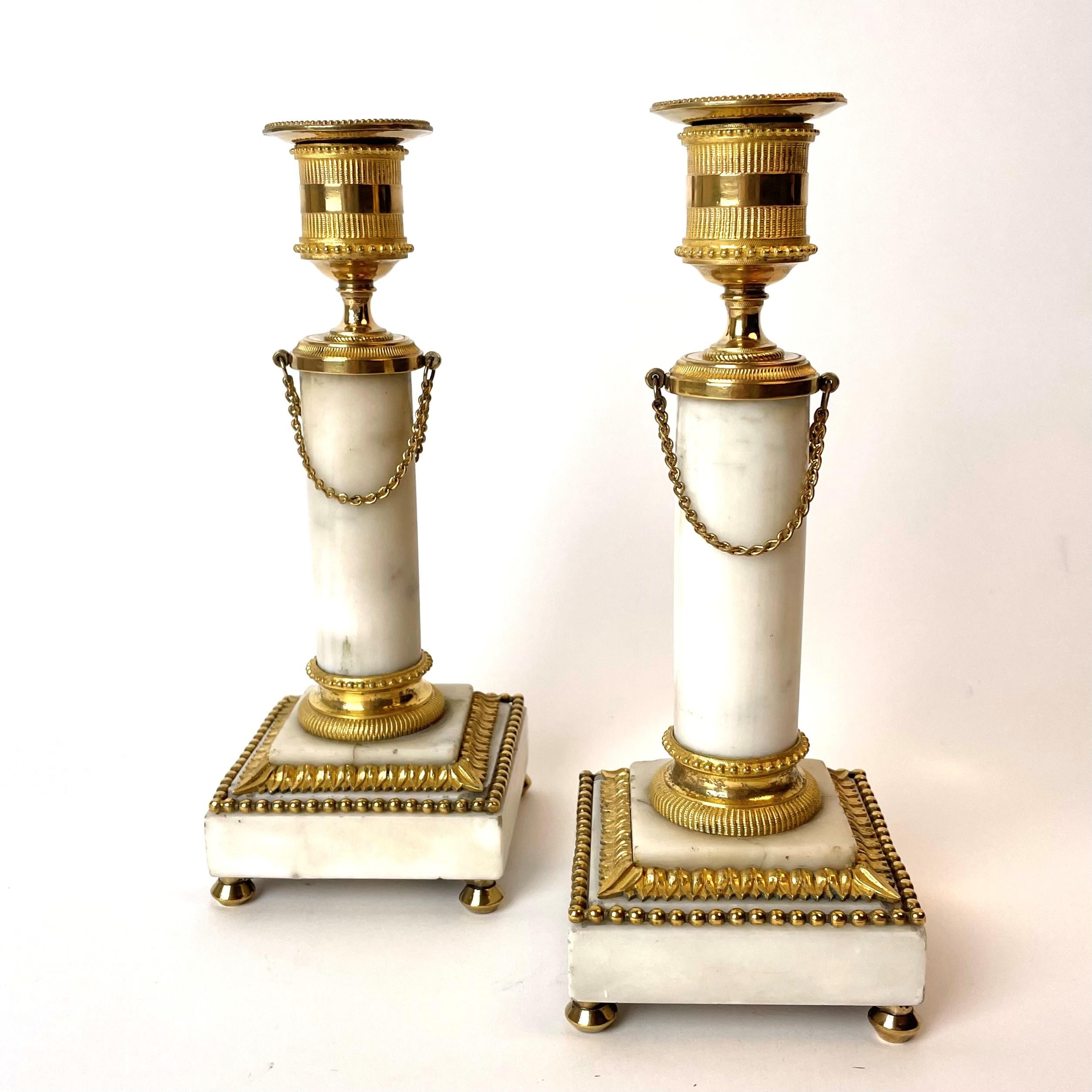A pair sophisticated carrara marble and gilt bronze Candlesticks. Made in France during the 1780s. Louis XVI.

Beautiful contrast between the white Carrara marble and the gilded decor.

There are some cracks in the marble (see pictures) and the