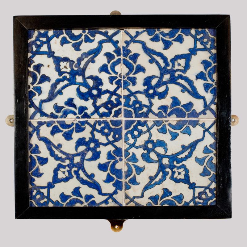A panel of four square Ottoman Empire ‘Dome of the Rock’ tiles, painted in underglaze cobalt blue with a trellis of split and winged palmettes with cloud-scroll collars, framed.  Syrian, 16th century.

15 in square, framed 17 ½ in