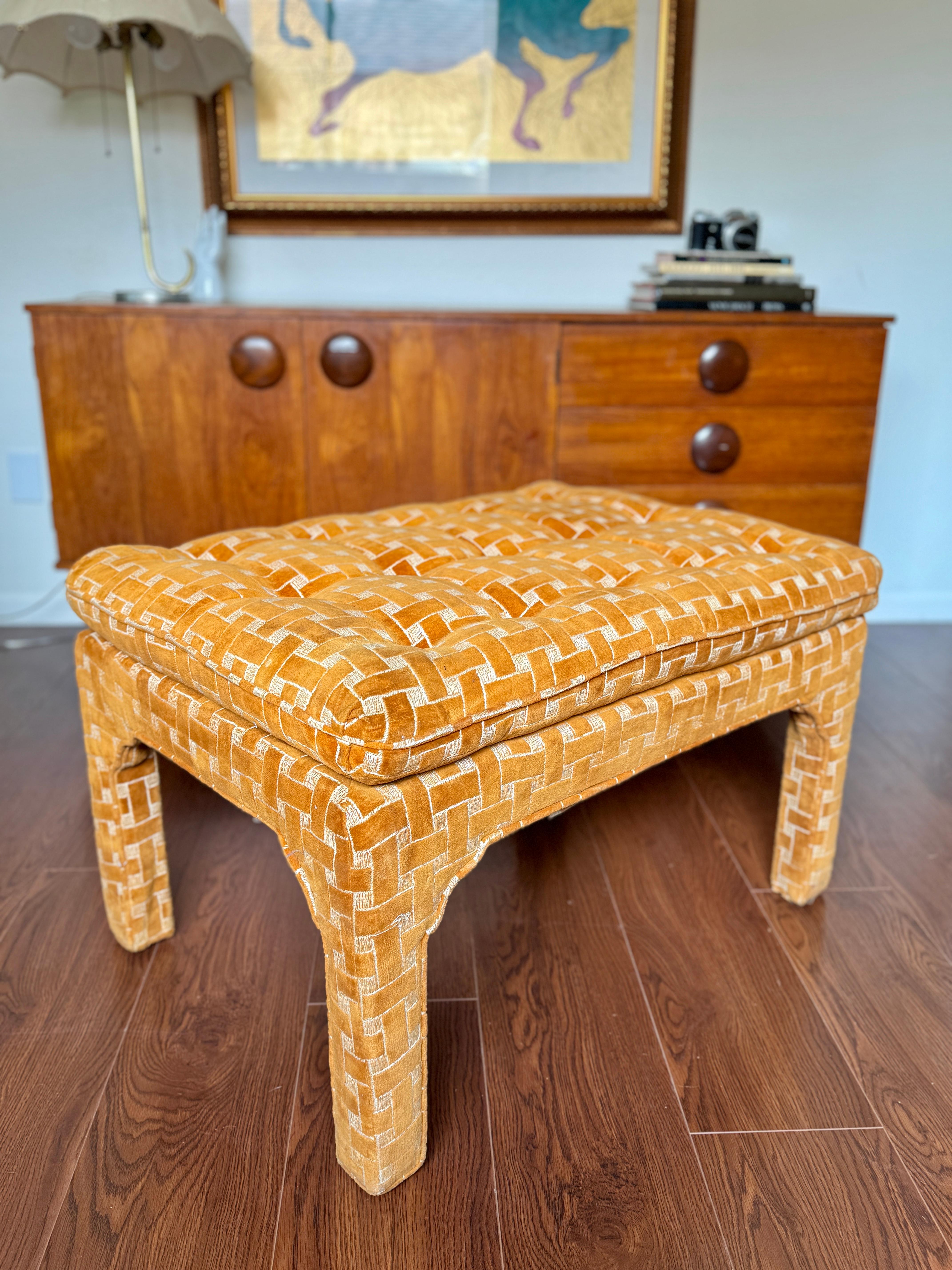A parson style upholstered bench in the style of Milo Baughman, circa 1970s. This bench has a buttoned pillow top with upholstered legs featuring the original orange and white basket weave cut velvet upholstery. In good original condition with no