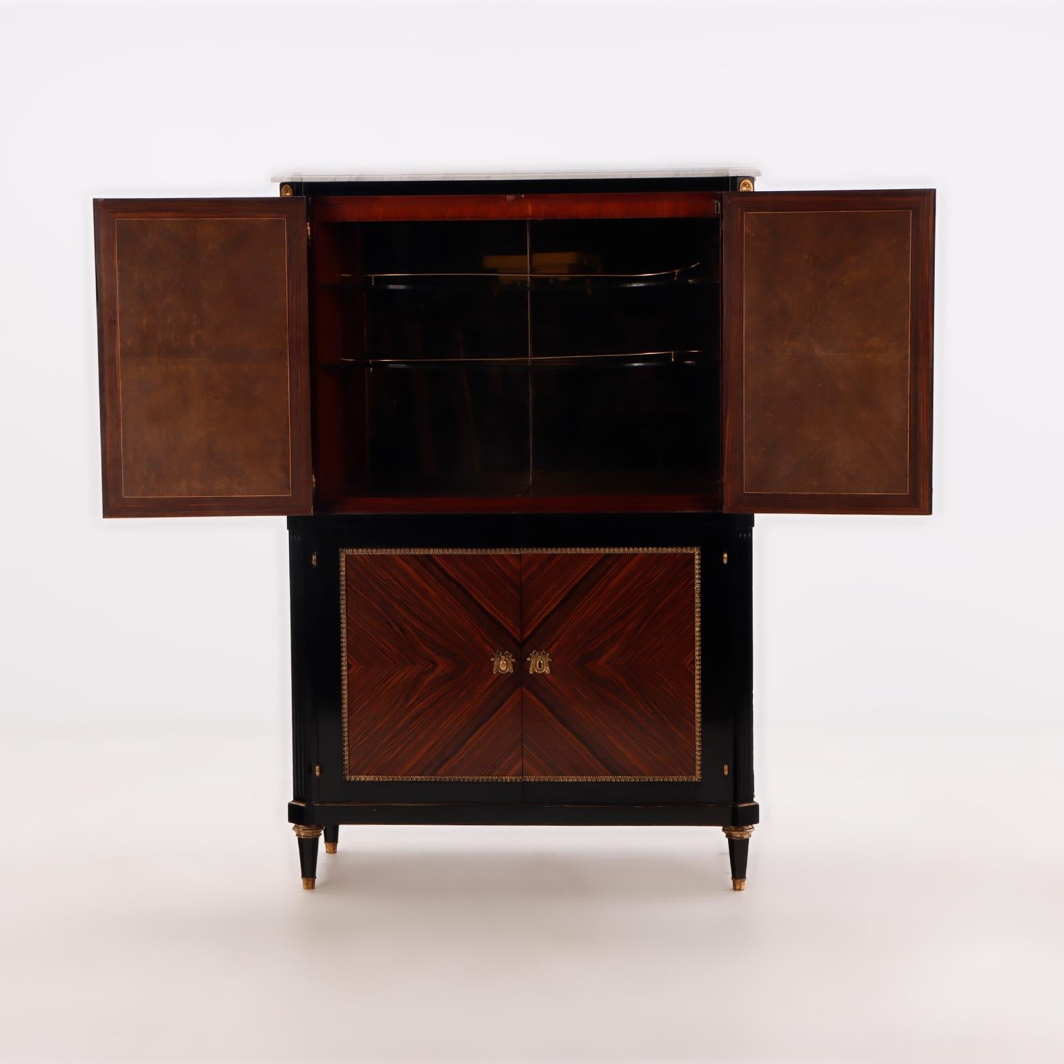 A partial ebonized four door bar cabinet in the manner of Jansen circa 1940. Having a marble top. The upper section has a mirrored back designed to hold glasses. 