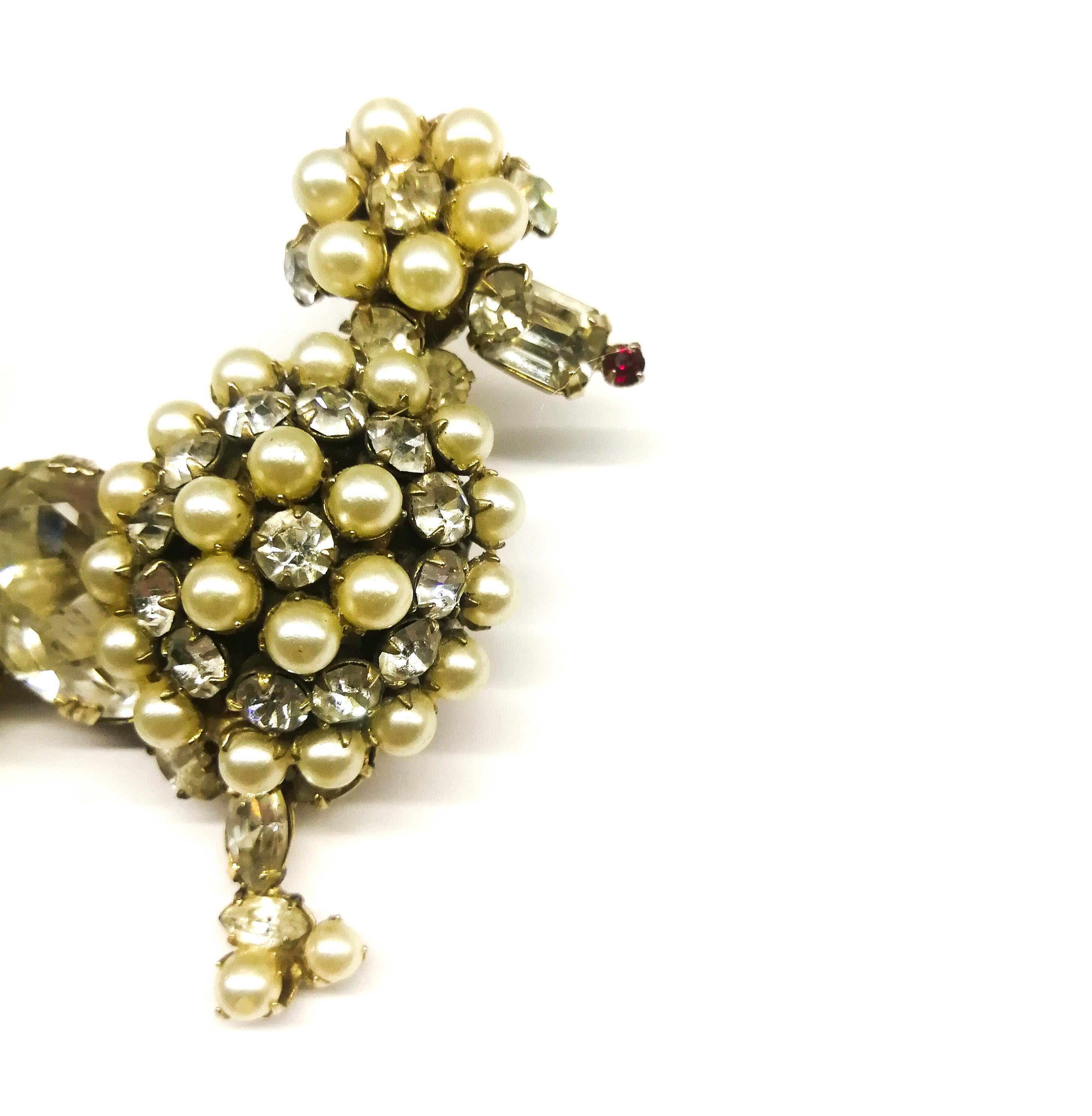 A charming and amusing clear paste and paste pearl brooch, in the form of a 'poodle. Beautifully modeled, with a small red nose as a highlight, and a single pearl atop its tail, a large clear stone as its body, the pearl and paste combination make a