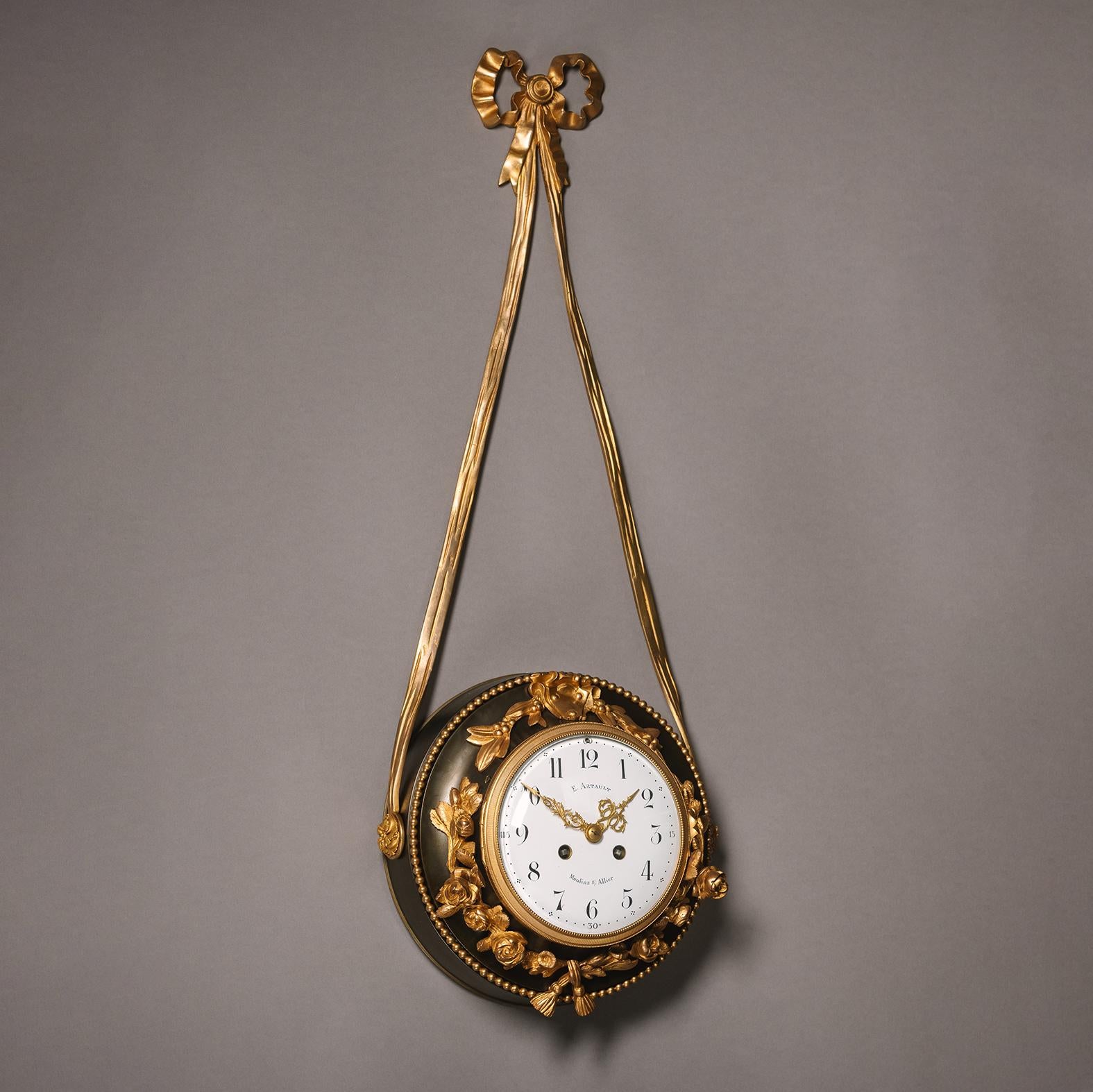 A Patinated and Gilt-Bronze Hanging Clock, with an enamelled dial and Arabic Numerals.

The dial signed 'E. Artult  / Moulins S.Allier'. 

The clock with a twin-train movement and a white enamelled dial with framed by gilt-bronze rock roses and