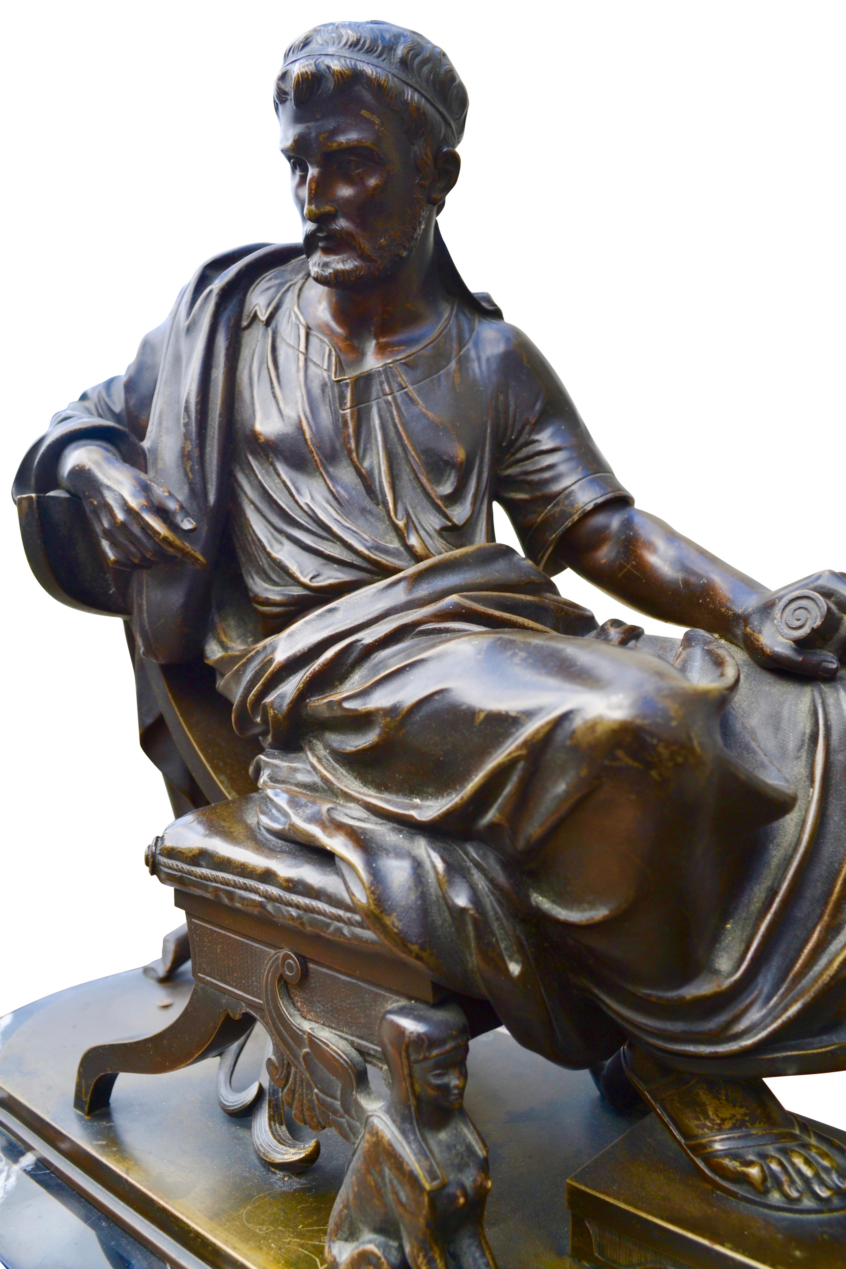The bronze statue features a Greek or Roman philosoper sitting/leaning back on his klismos chair which has two winged griphons as front leg supports. He is fully draped in his toga, his right arm is relaxed and held over the back of his chair, his