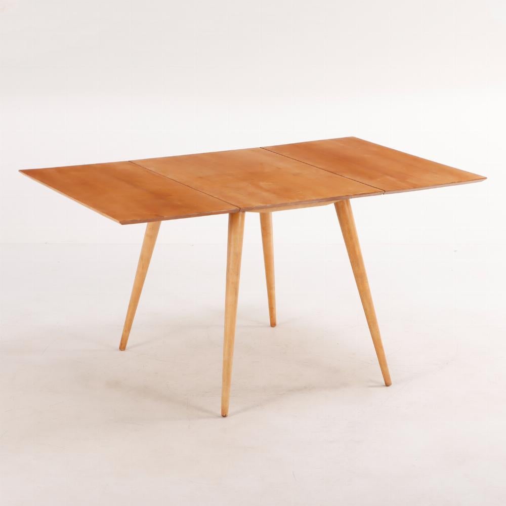 A Paul McCobb (American, 1917-1969), maple drop leaf dining table circa 1950. A gorgeous slender top supported by tapered and splayed legs. 
Drop leaves are 17