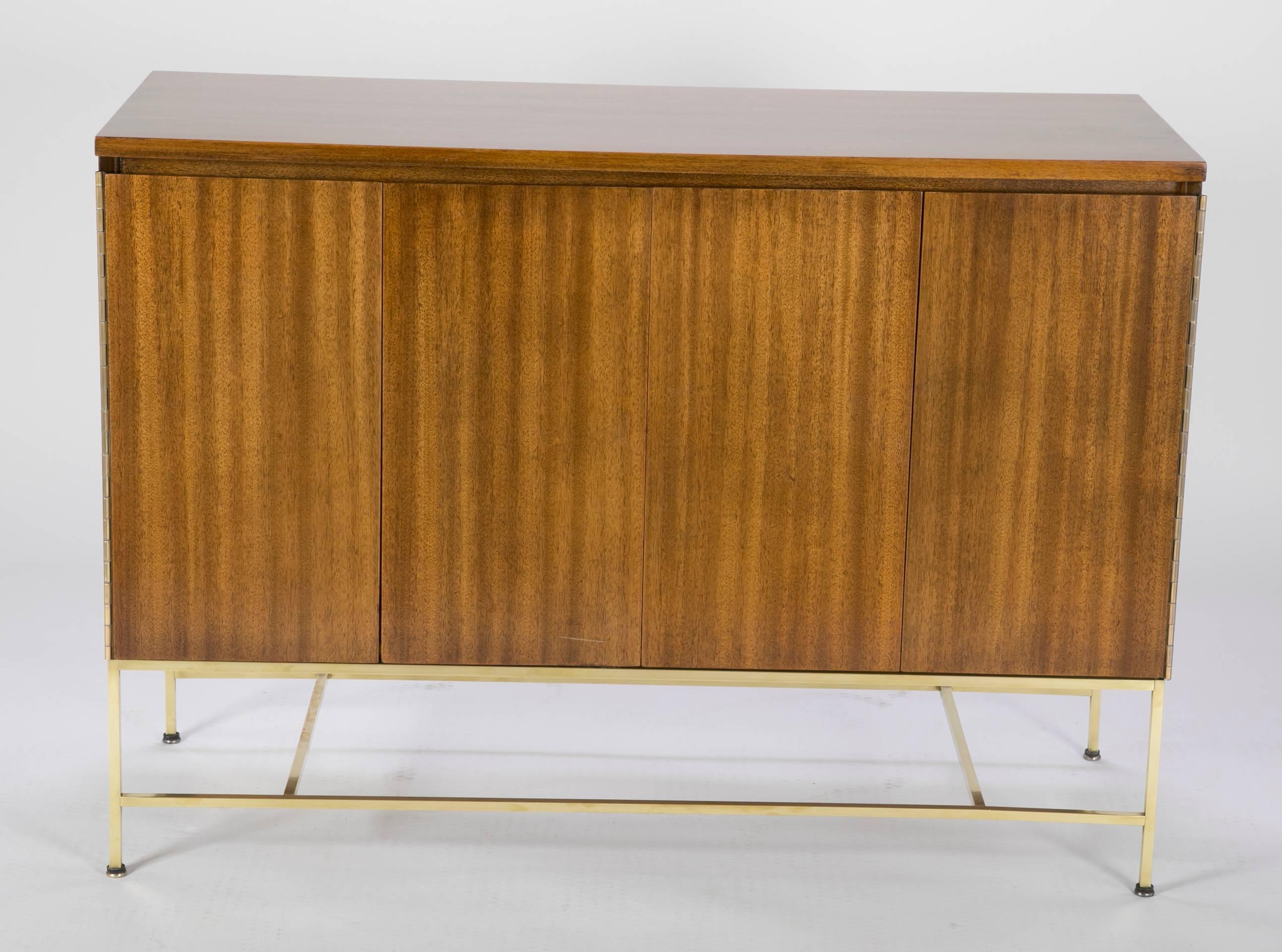 A Paul McCobb chest with two screen fold walnut doors revealing two set of shelves. The case is set over a brass armature. Model 7303.