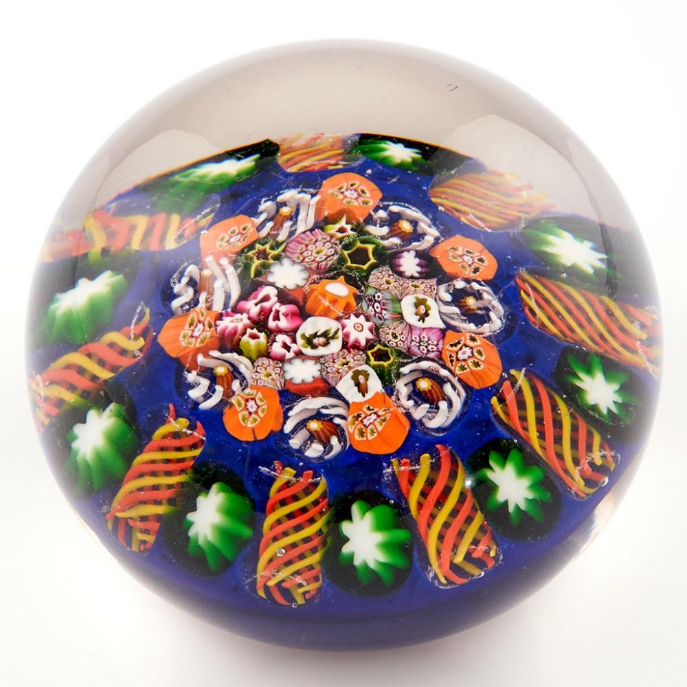 A Paul Ysart Close Pack Radial Paperweight, c1950

Additional information:
Date : c1950
Origin : Scotland
Features : A close pack of complex millefiori canes surrounded by a 9 spoke radial concentric ring
Marks : Unusual marks to the base maybe