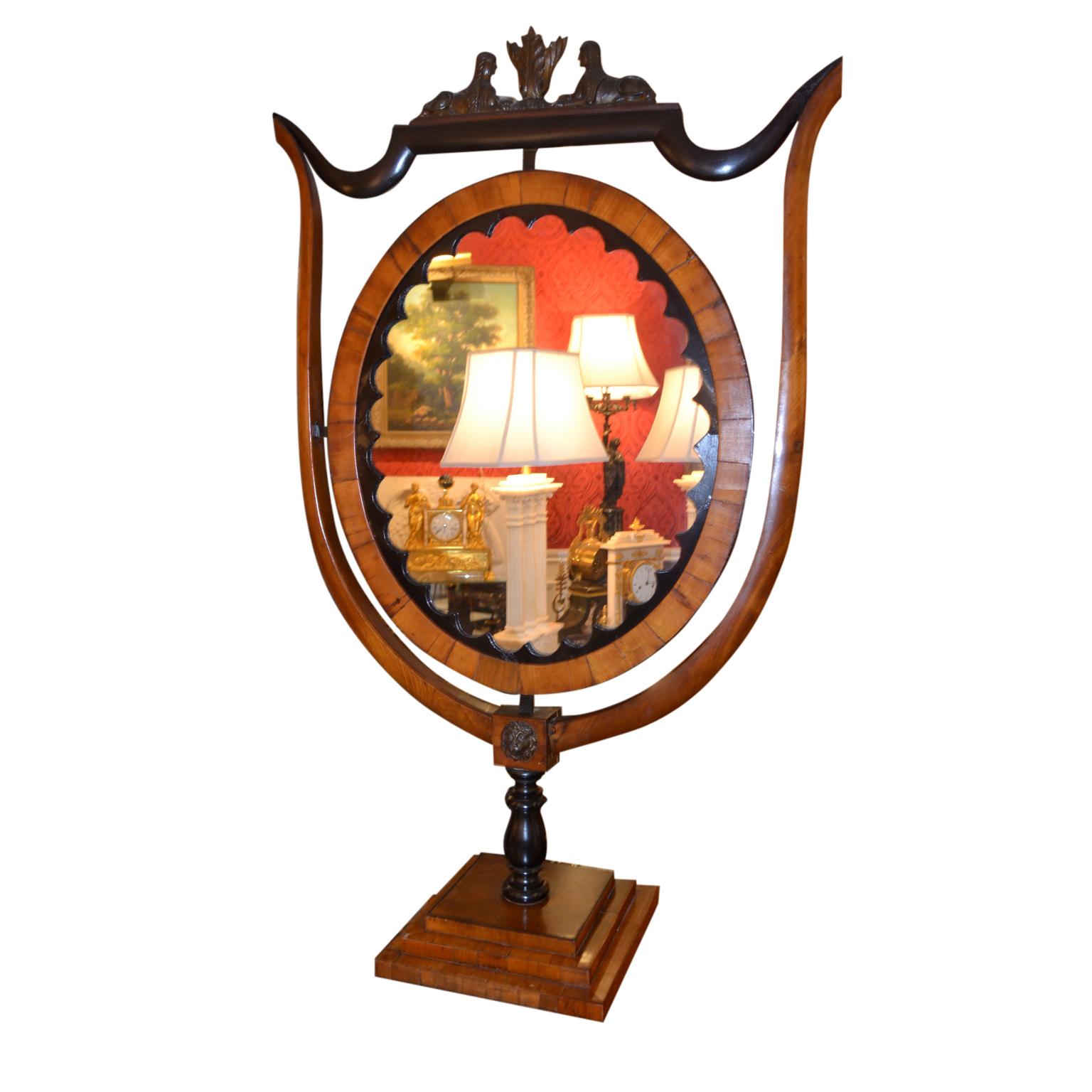 A rare Biedermeier standing table mirror in ebony and fruitwood. The shield shaped frame is supporting an oval mirror surmounted by two facing ebonized Egyptian sphynx. The whole is supported on a stepped rectangular base. It does not swivel.