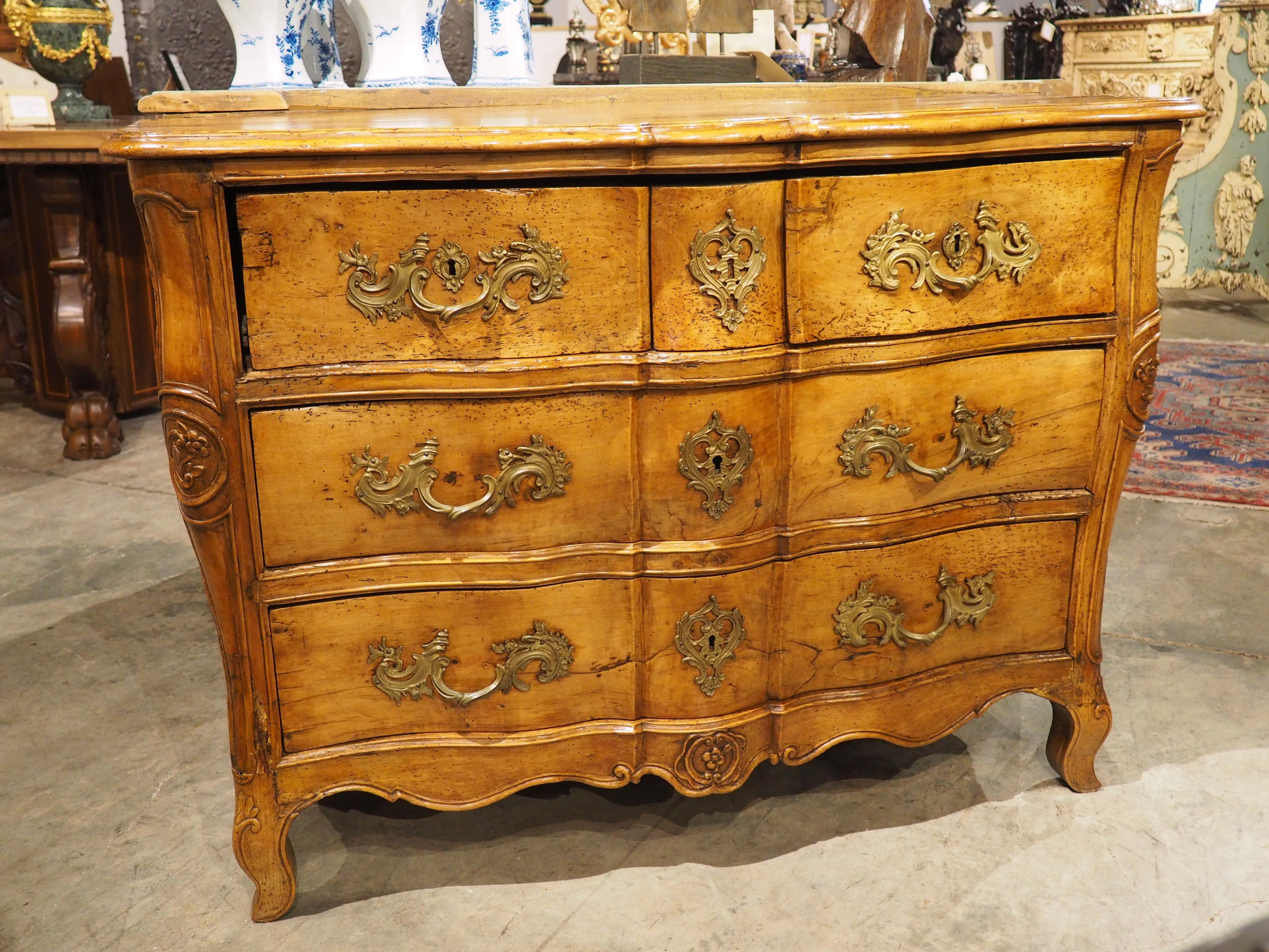 Il legno di noce biondo di questa commode galbé francese ha una tonalità calda, color miele, accentuata dalla ferramenta in bronzo dorato. Intagliato a mano nel 1750 circa, questo bellissimo cassettone risale al periodo di Luigi XV, come dimostrano