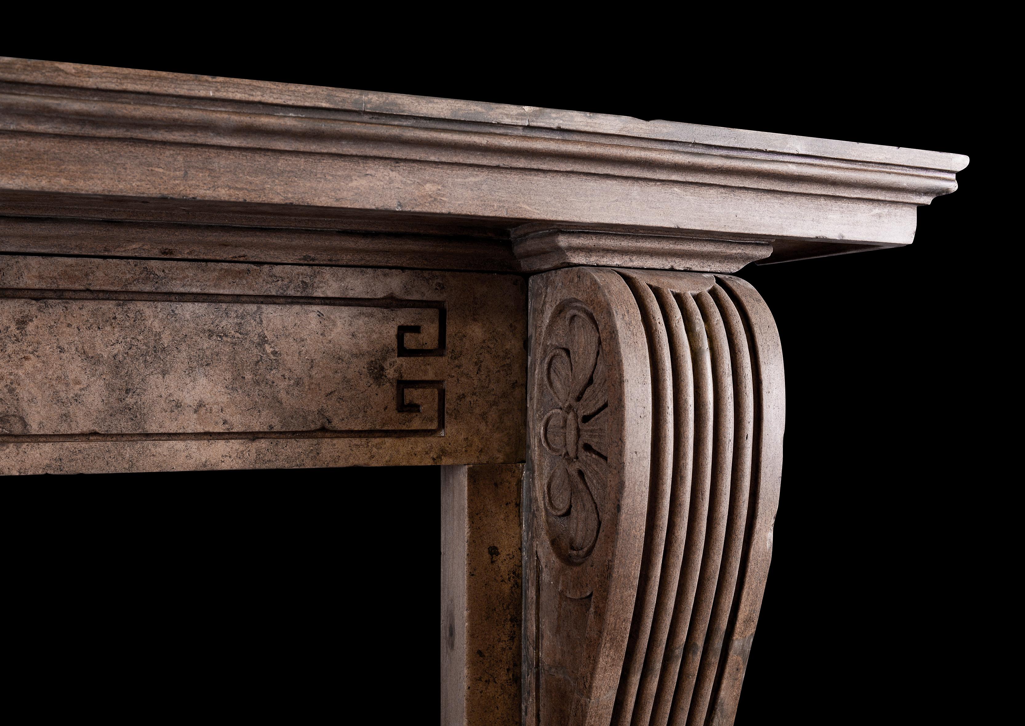 Une grande et impressionnante cheminée d'époque en pierre de style Régence. Les jambages profilés et cannelés sont surmontés de consoles sculptées et de rondeaux sur les plinthes. La frise à motif de clé grecque, surmontée d'une tablette moulurée.