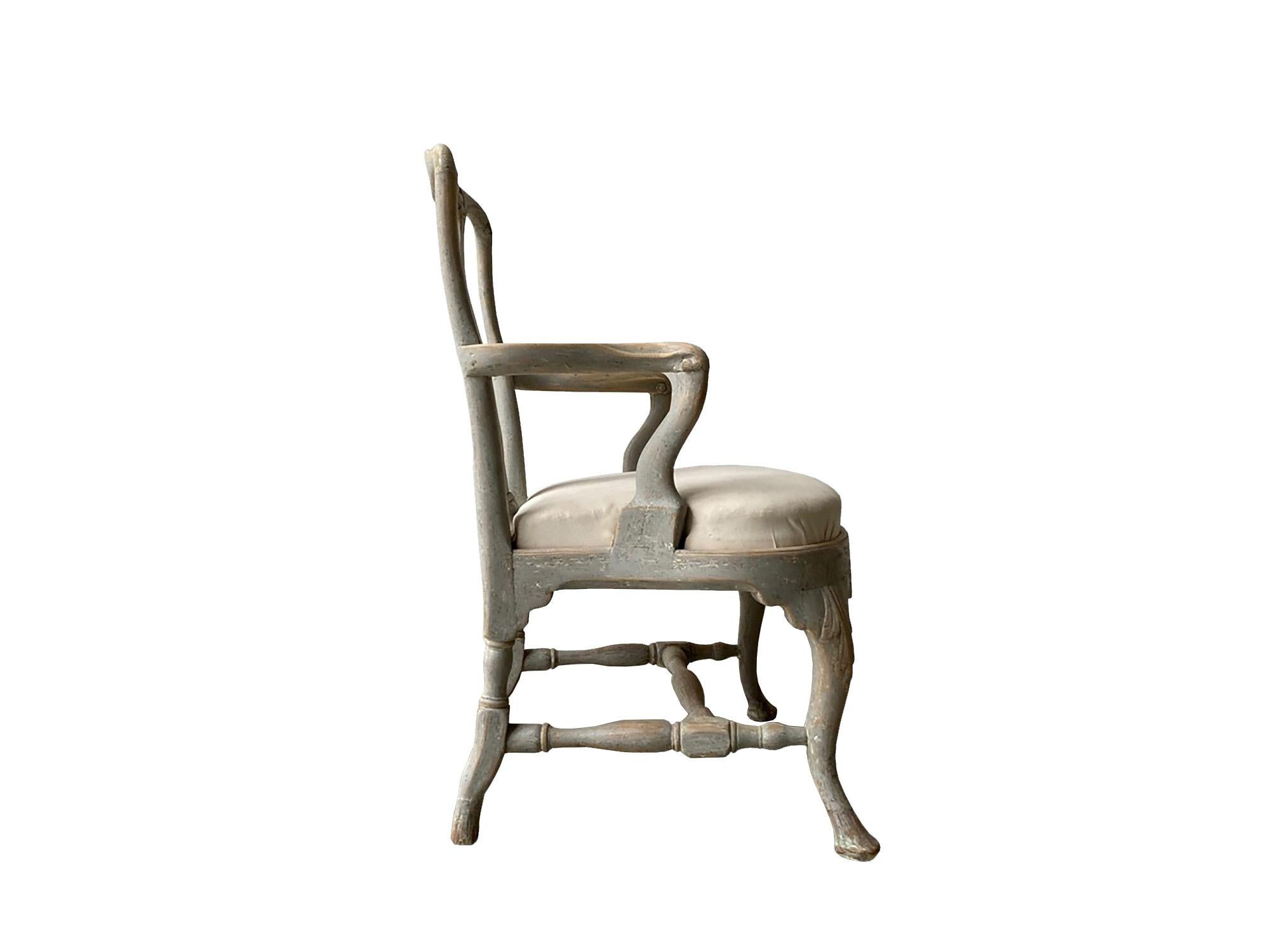 A period Swedish Rococo armchair with decorative carved shell detail in the back and seat stretcher. This piece has been repainted in light greenish grey and the seat has been reupholstered.