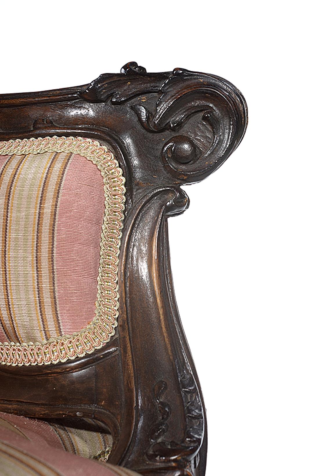 The walnut frame with carved acanthus leaves and bell flowers, the back, side panels and seat all upholstered in a pink and cream striped fabric.
The whole raised on cabriole legs that end on scroll feet.
 