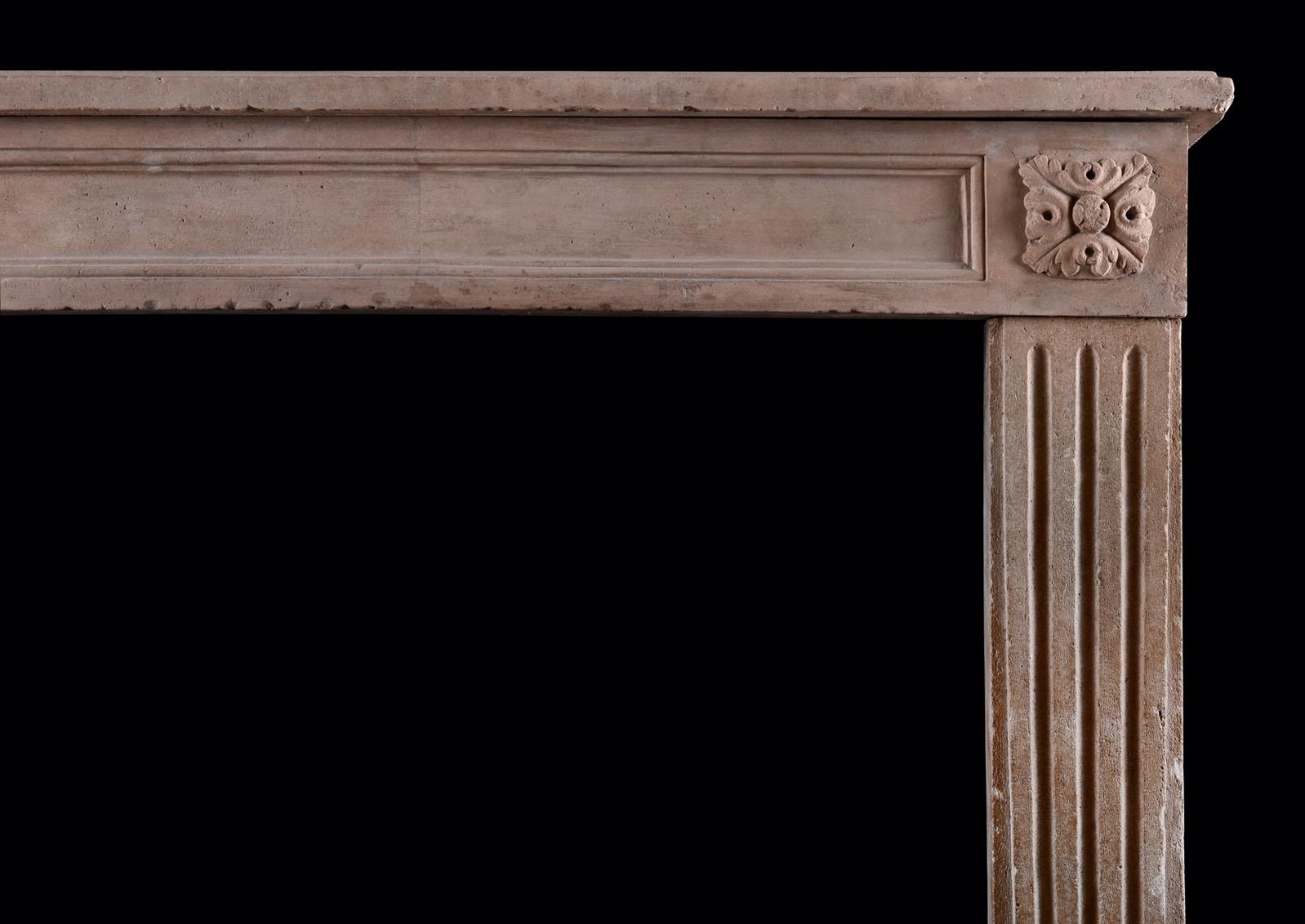 A petite French limestone fireplace in the Louis XVI manner. The jambs with tapering stop-fluted pilasters, the frieze with central panel flanked by carved paterae. Scalloped shelf above. A small scale, well suited for bedroom or smaller study.