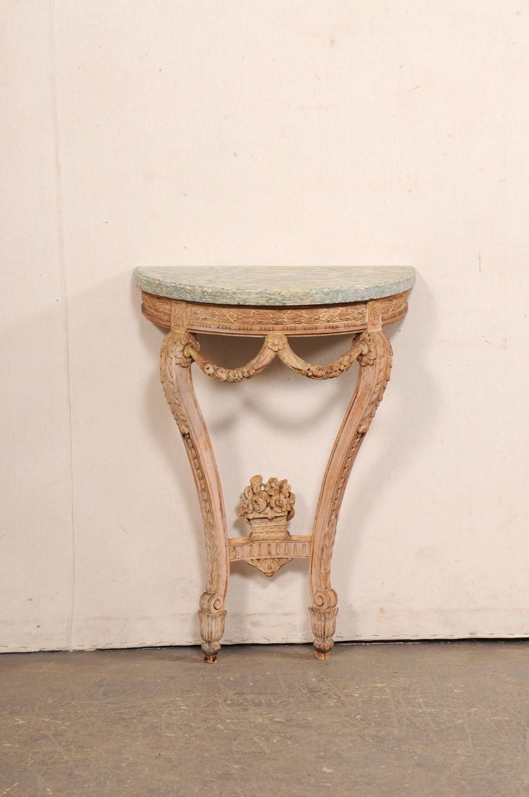 A small-sized Italian Neoclassic style elaborately-carved wood console table, with marble top, from the early 20th century. This antique table from Italy features a half-moon/demi-shaped marble top, which rests atop an apron which has been