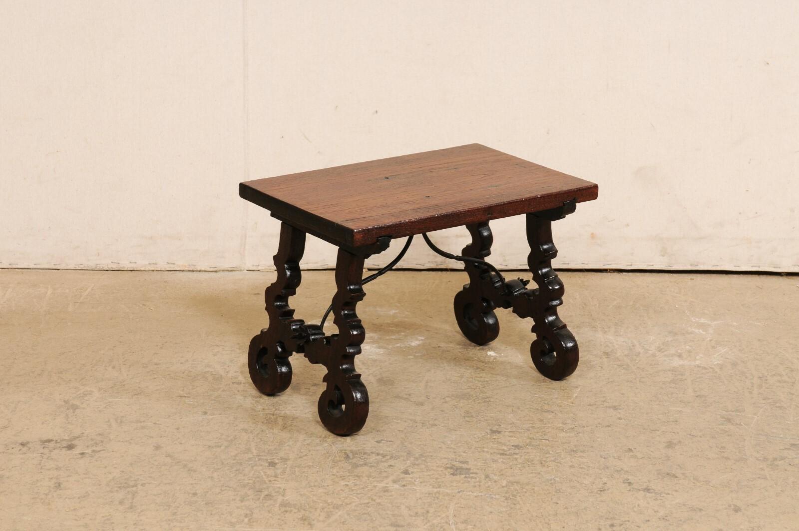 A Spanish carved-wood trestle-leg drinks table. This vintage small-sized table from Spain features a rectangular-shaped top which is raised upon a pair of sinuously carved lyre-legs with volute curled feet. The trestle legs are braced with an iron