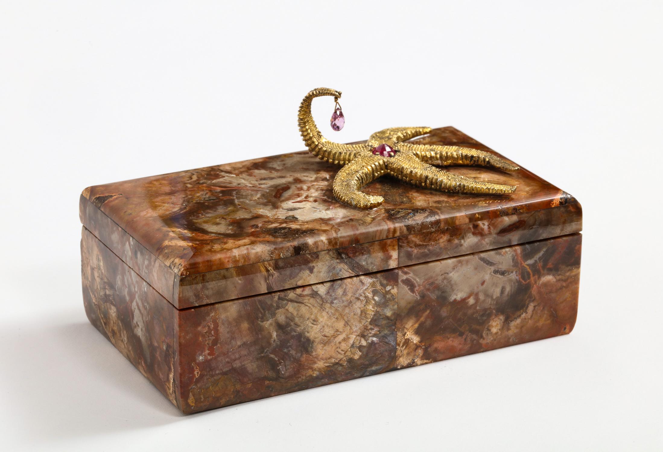 A petrified wood box with silver-gilt starfish and pink sapphire by Nardi,
Venice, Italy, 20th century.

Comprised of finely polished petrified wood chosen for their exceptional color and patterns, the lid mounted with a large silver gilt