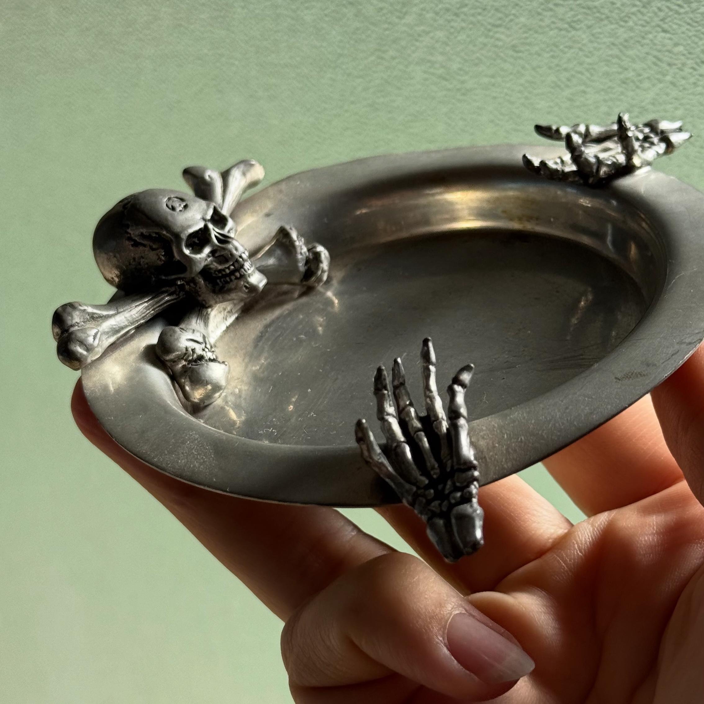 An ashtray delicately crafted of pewter featuring skull and crossbones and skeleton hands by Alchemy Pewter, Sheffield England 20th century. Gorgeous craftsmanship and maker’s mark on verso of piece. 