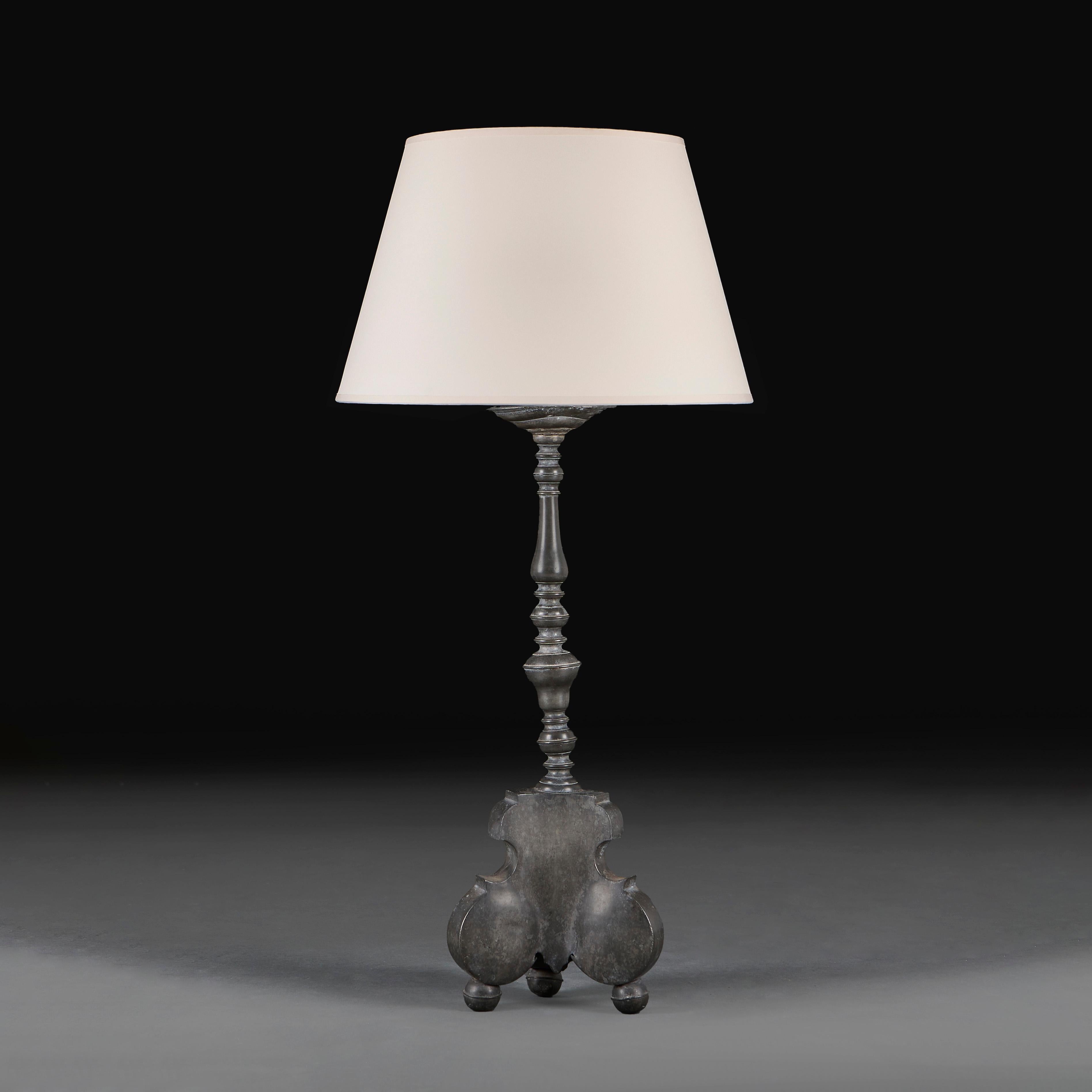 A French eighteenth century pewter candlestick of large scale, with baluster stem and shield form tripod base, supported on three ball feet, now as a lamp. 
Height of candlestick    61.50cm
Height with shade   90.50cm
Width of base   22.00cm
France,
