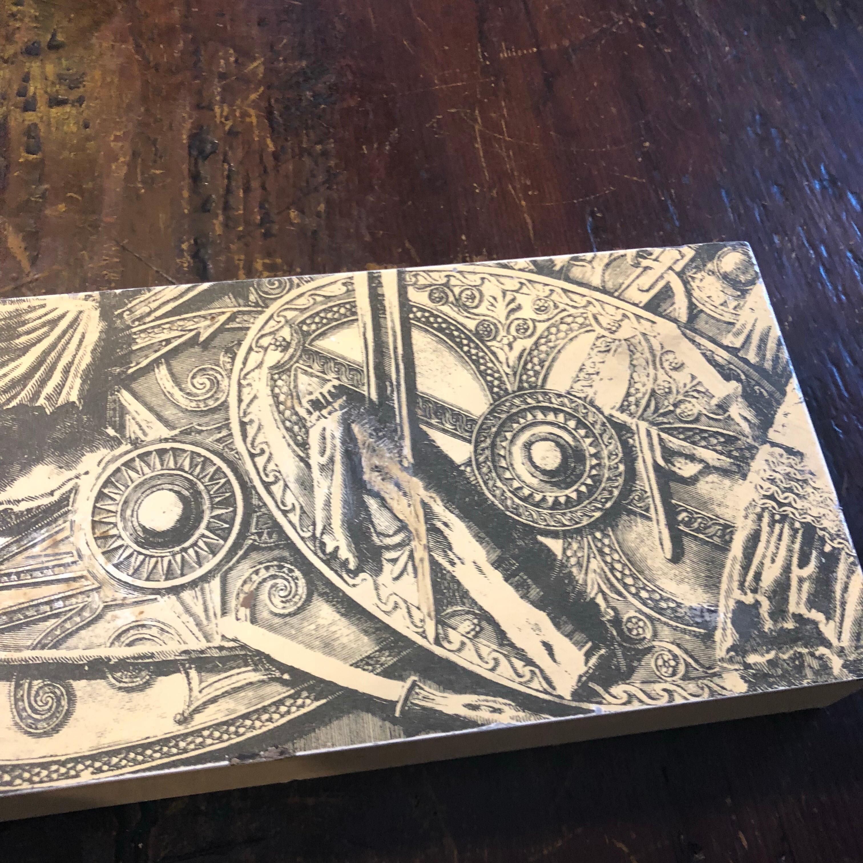 A box designed by Piero Fornasetti and manufactured by Atelier Fornasetti, It has an ivory metal cover with black patterns typical of Piero Fornasetti and a mahogany inner compartment. Good conditions overall, signs of use and age.