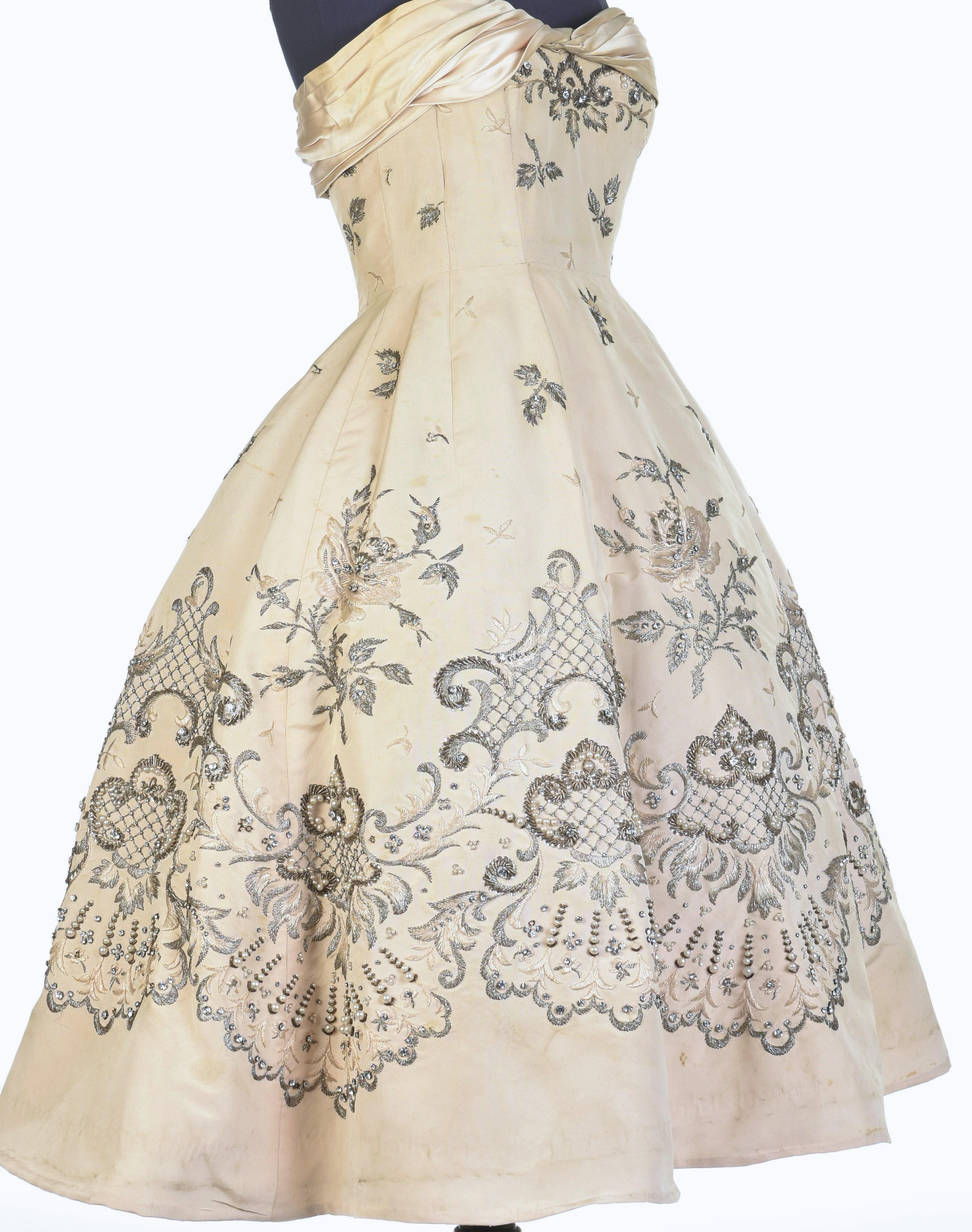 Circa 1955/1957

France

Majestic cocktail or ball gown in silk ottoman embroidered Champagne by Pierre Balmain Haute Couture numbered 87681, model Versaille. Sheath dress with large plunging neckline with bare back, accented with a drape, pleated