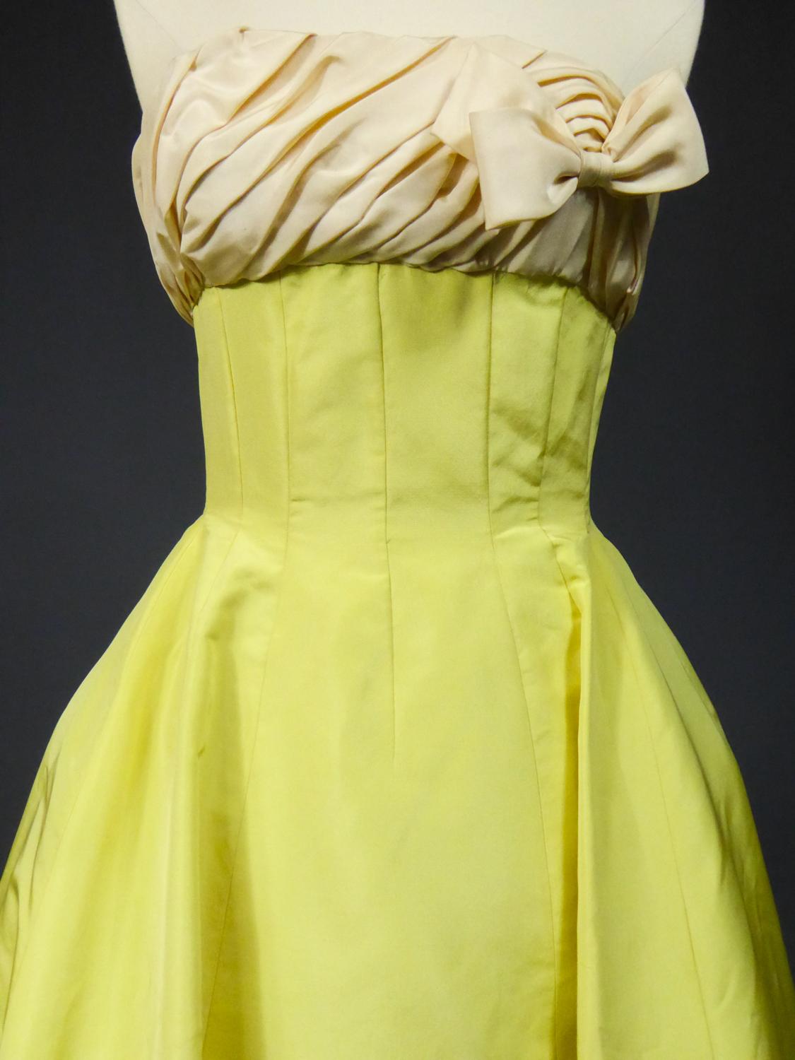 Circa 1958

France

A yellow banana ottoman silk faille ball-gown or ceremonial long dress. Boned bodice with large plunge neckline and cream oblique pleated shape faille on the chest adorned with a side knot. High waist effect obtained by a high
