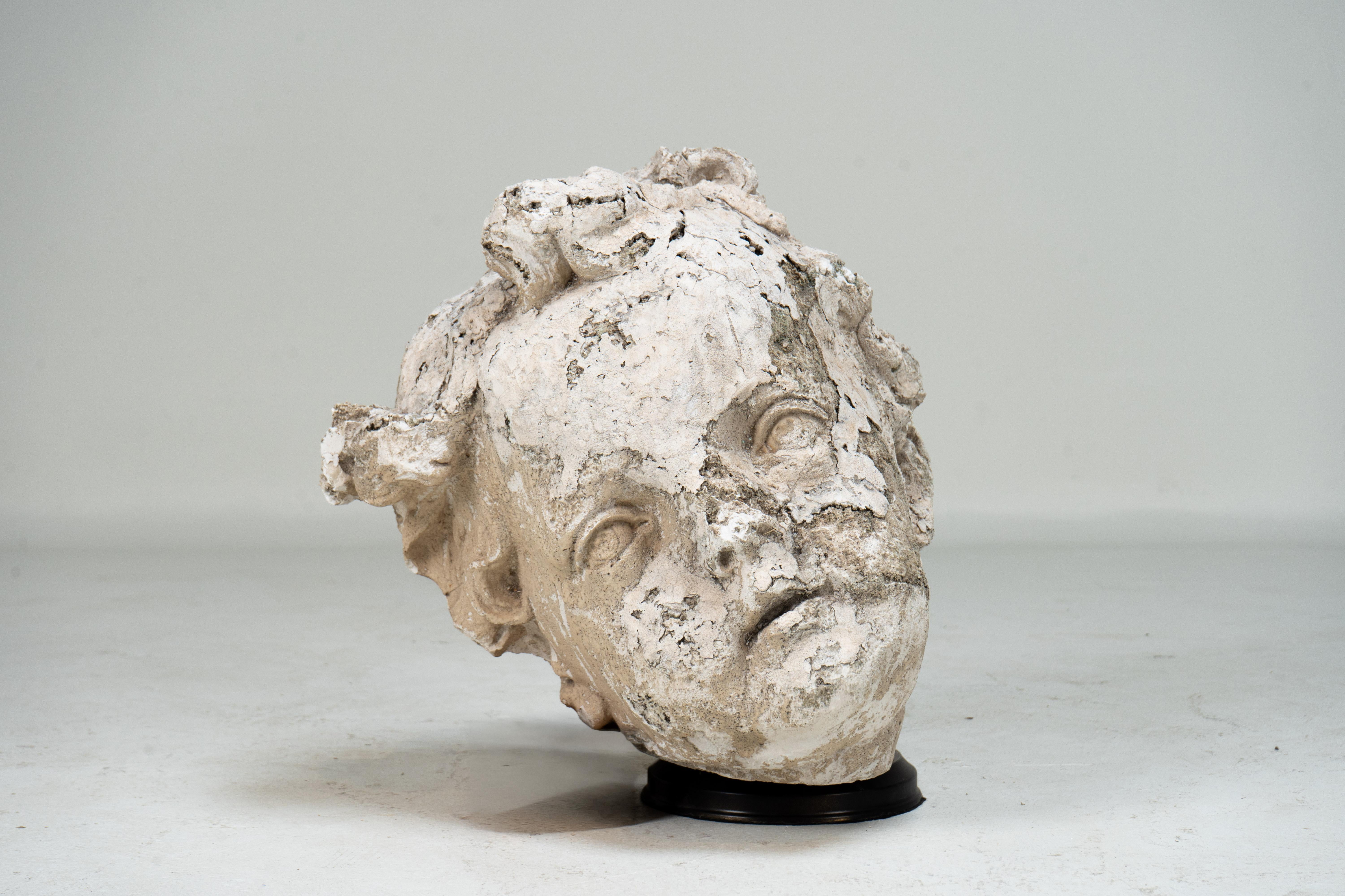 Tête d'angelot en plâtre datant d'environ 1900. Cette sculpture évocatrice capture les traits doux et l'expression délicate d'un nourrisson dans le style classique. La surface présente une belle patine d'usage. Probablement une partie d'un élément