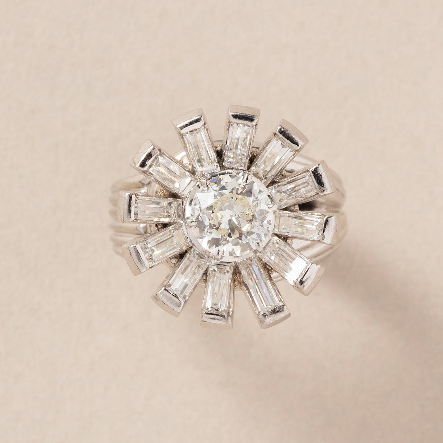 A platinum and 18 carat white gold ring with an asymmetrical ribbed shank set with an old cut diamond (0.9 H, Si2) in the heart and 12 baguette cut diamonds around as a flower (12 x 0.2 krt G-H Si), circa 1950.

weight: 13 g
diameter: 1.7 cm
ring