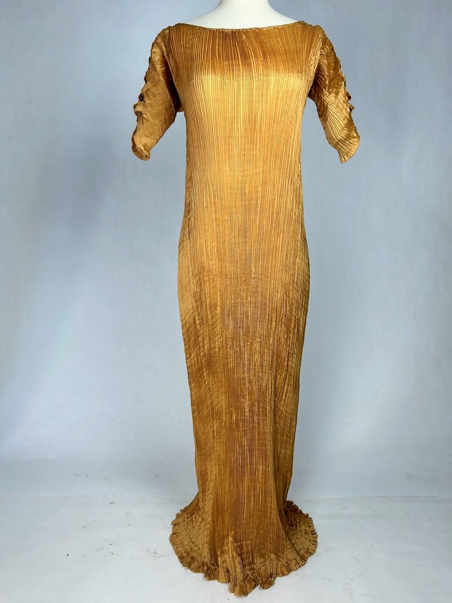 Circa 1920-1930
Italy - Venice
Delphos long dress in apricot-coloured pleated silk pongee by the famous Italian couturier Mariano Fortuny (Attributed to). Straight, tubular cut in four hand-sewn panels, extending to the floor. Short sleeves