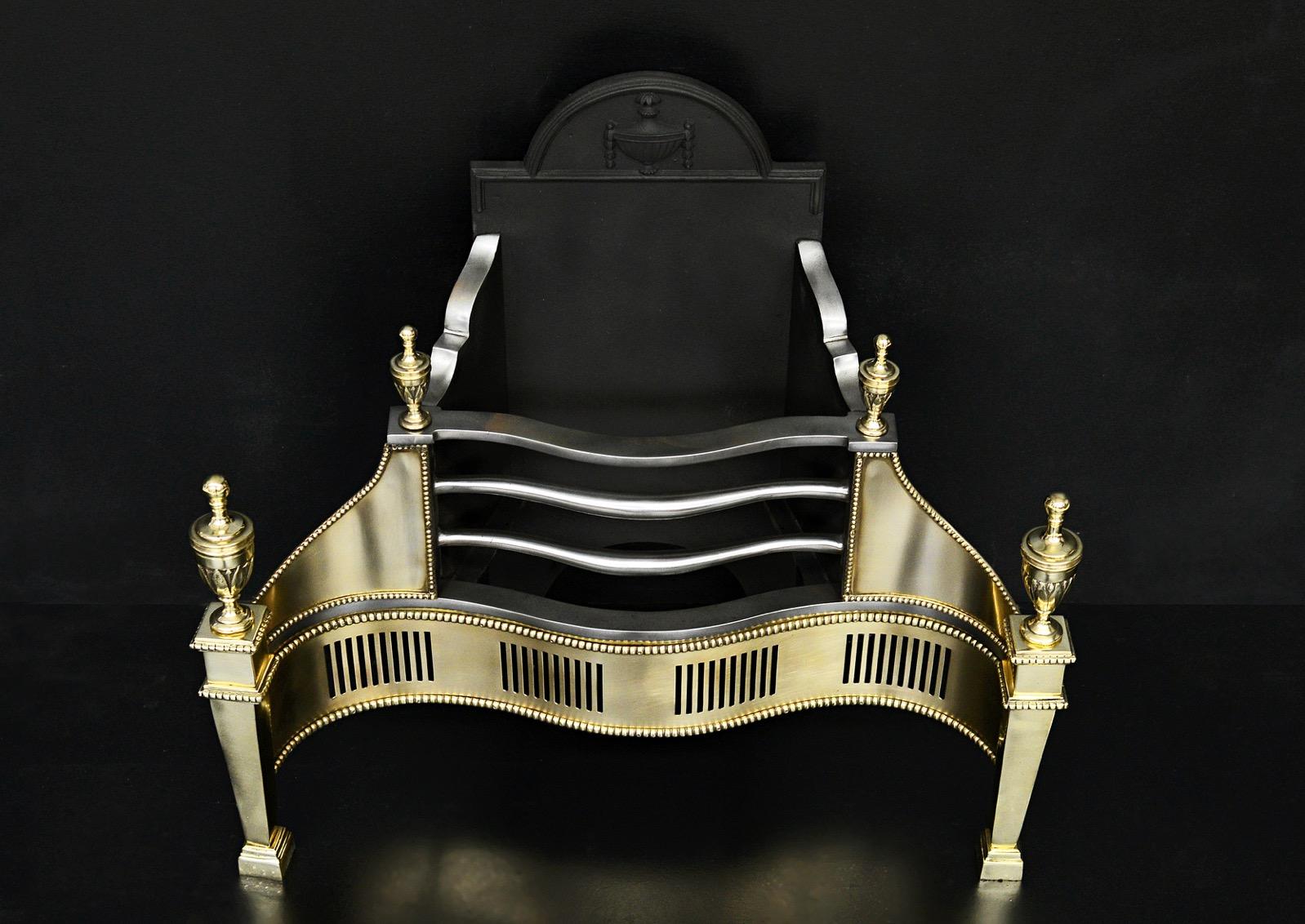 A polished brass firegrate in the Georgian manner. The serpentine, pierced fret with beading above and below surmounted by polished steel bars with and urn finials. The tapering legs with larger matching urn finials above. Decorative cast iron back