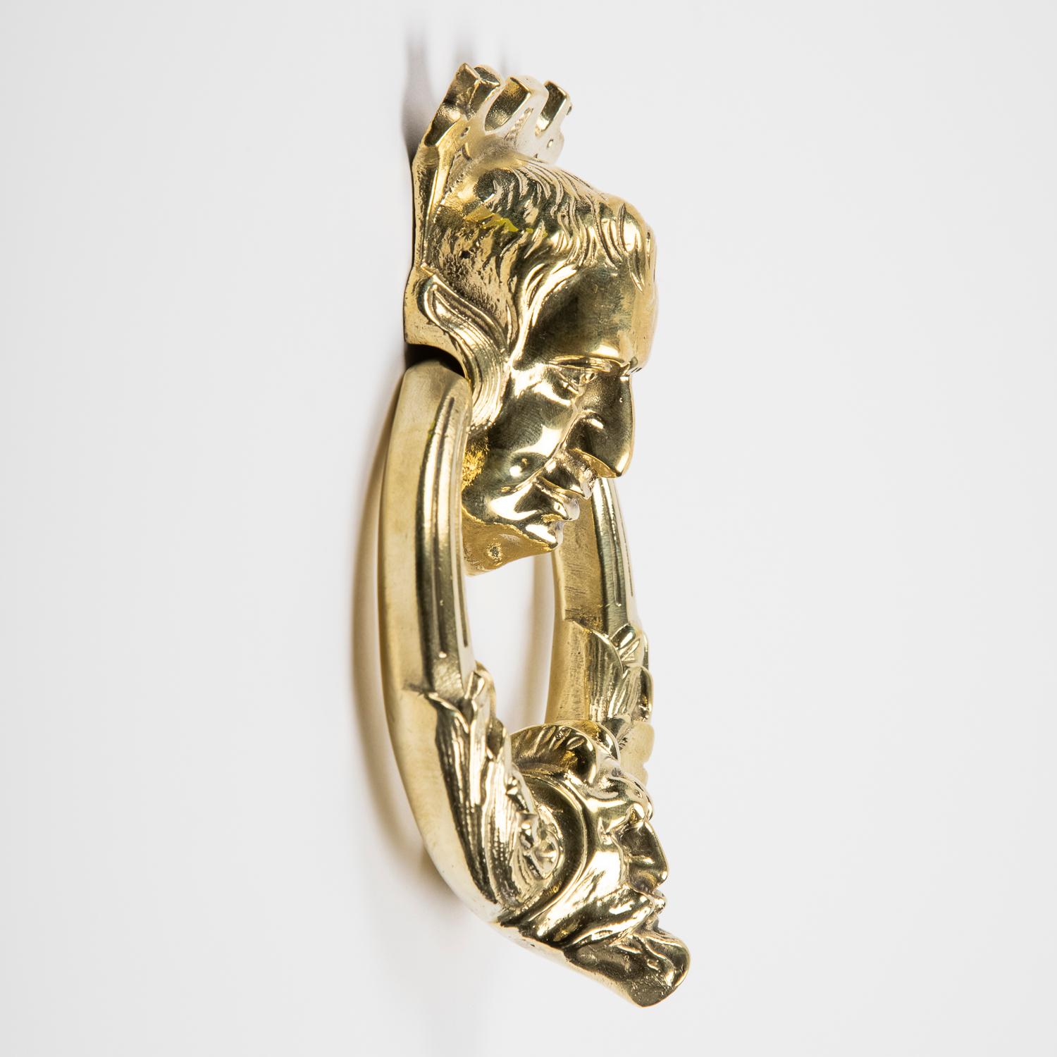 A polished bronze door knocker, with two men's faces.

Projection: 4 cm.