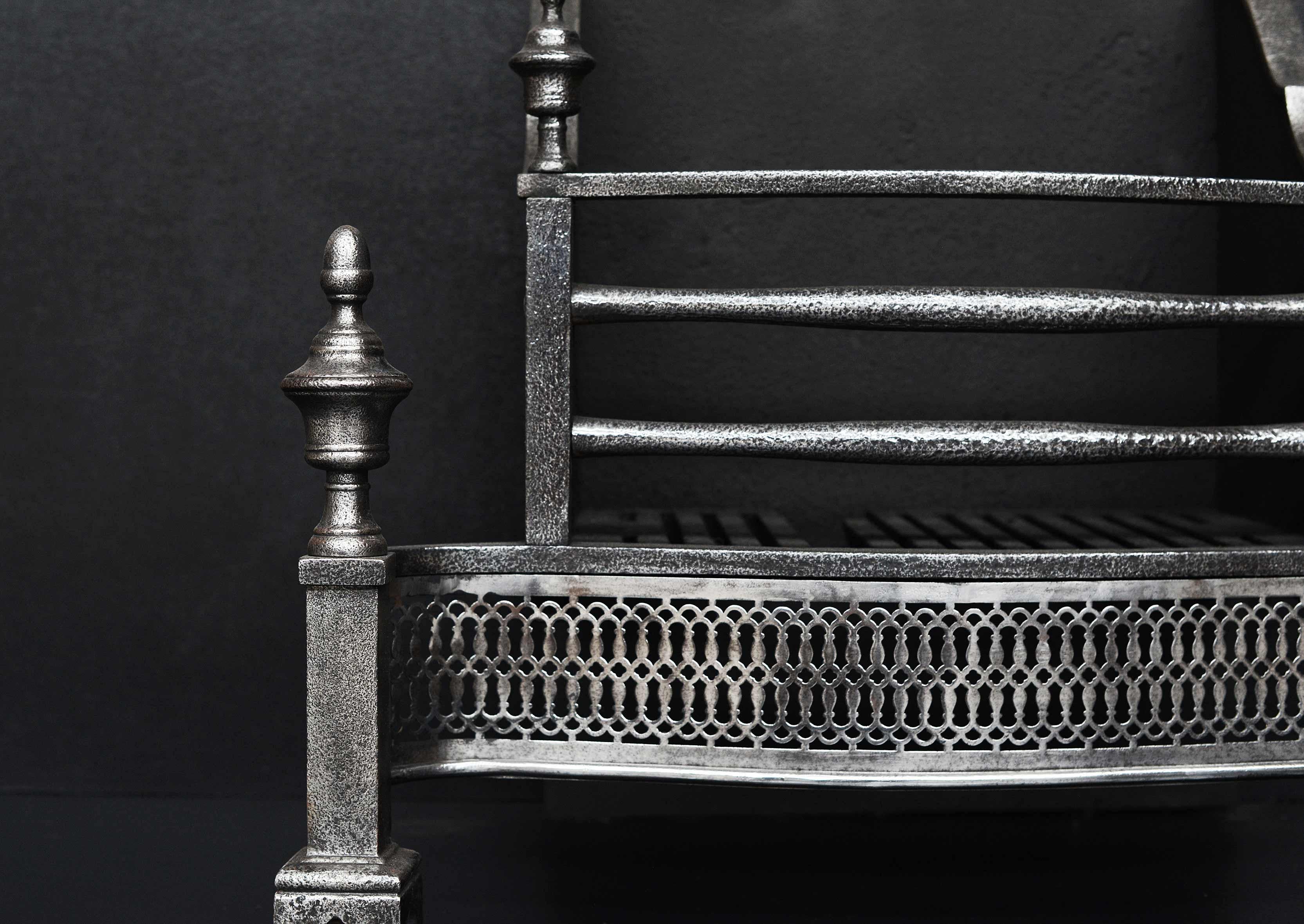 A polished iron firegrate in the Georgian style. The square legs surmounted by urn finial, the burning area with shaped front bars and pierced fret below. Plain cast iron fireback behind. English, 19th century with later additions.

Width at