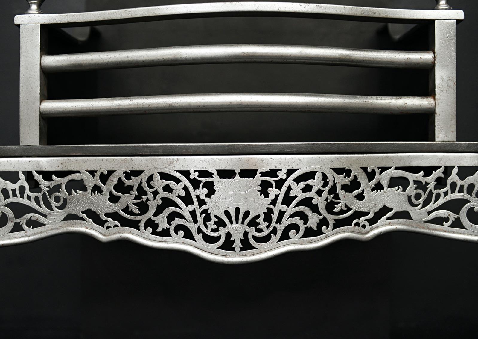 A polished steel firegrate in the Georgian style. The tapering, stop-fluted legs surmounted by classical urn. The pierced fret with mythical beasts and scrollwork throughout with bowed front bars above. English, 19th century. 

Width At Front:	767