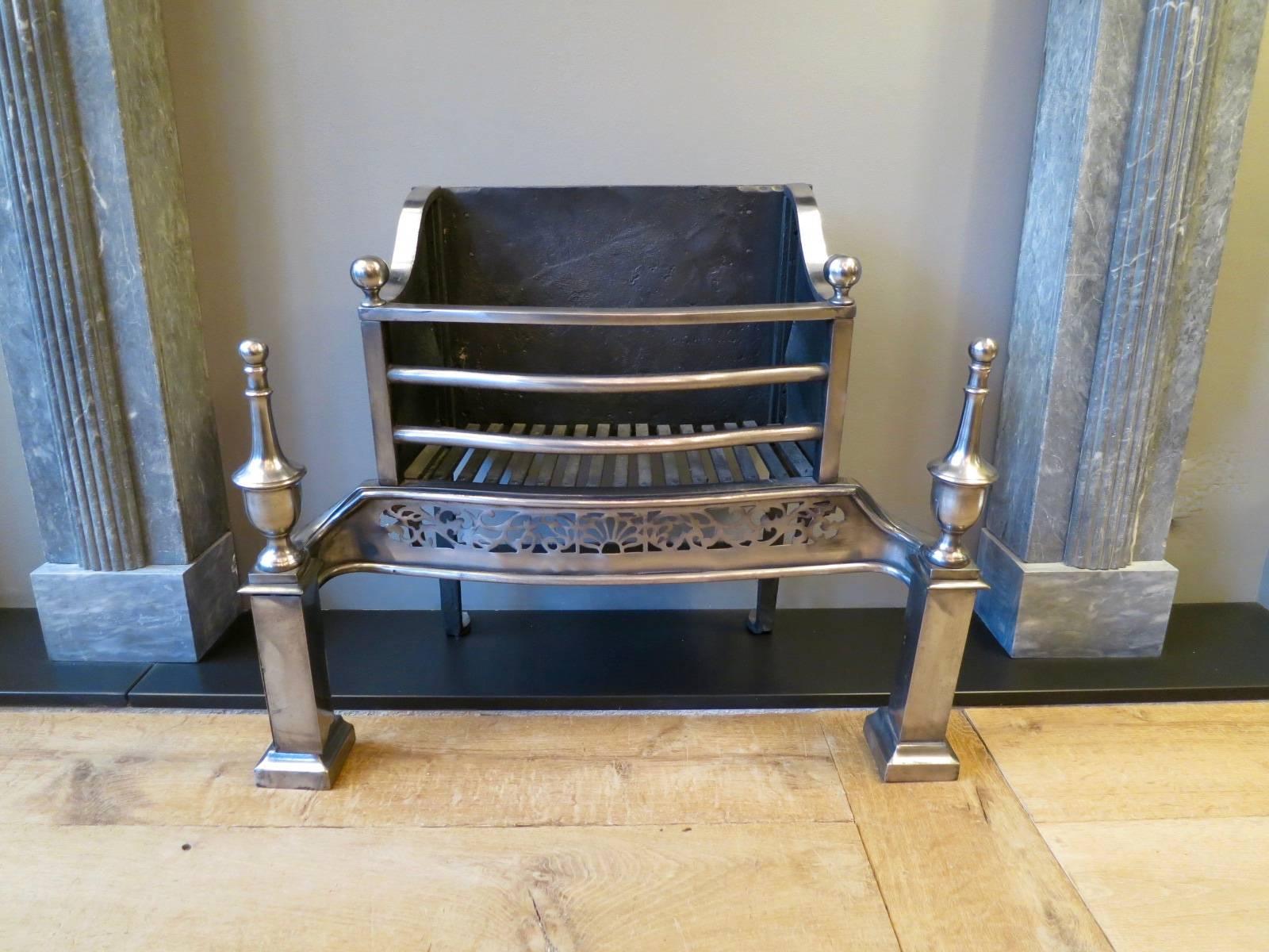 An English fire grate, in polished steel finish. The front columned supports surmounted by tall finials. The edged fret work of foliage and shell pattern, beneath gently curved bars with ball finials, late 19th century.
