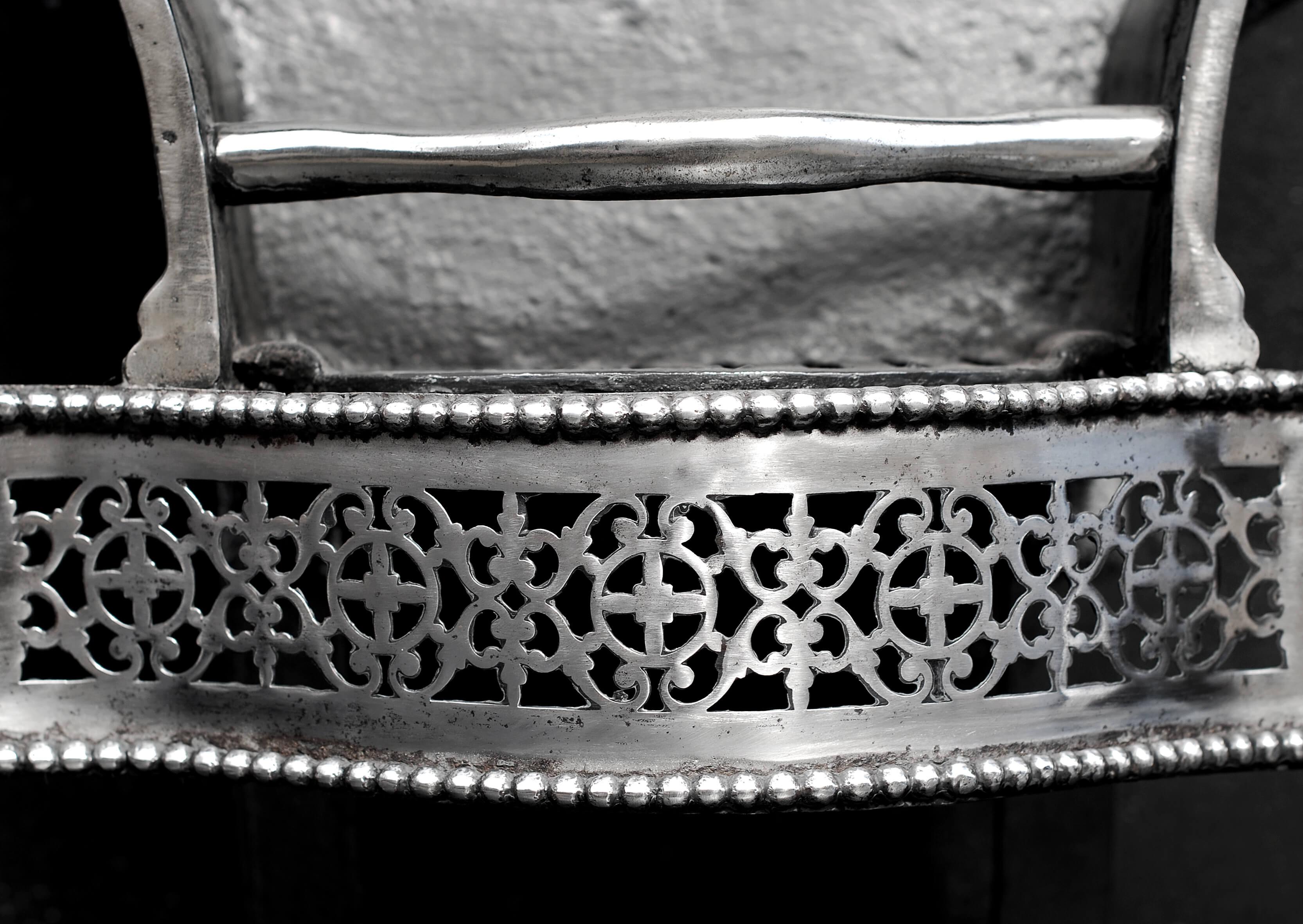 An English steel firegrate. The pierced, shaped fret with beading above and below surmounted by shaped front bars to burning area. The shaped legs with ball feet and steel finials. Shaped cast iron back. Late 19th / early 20th century.

Measures: