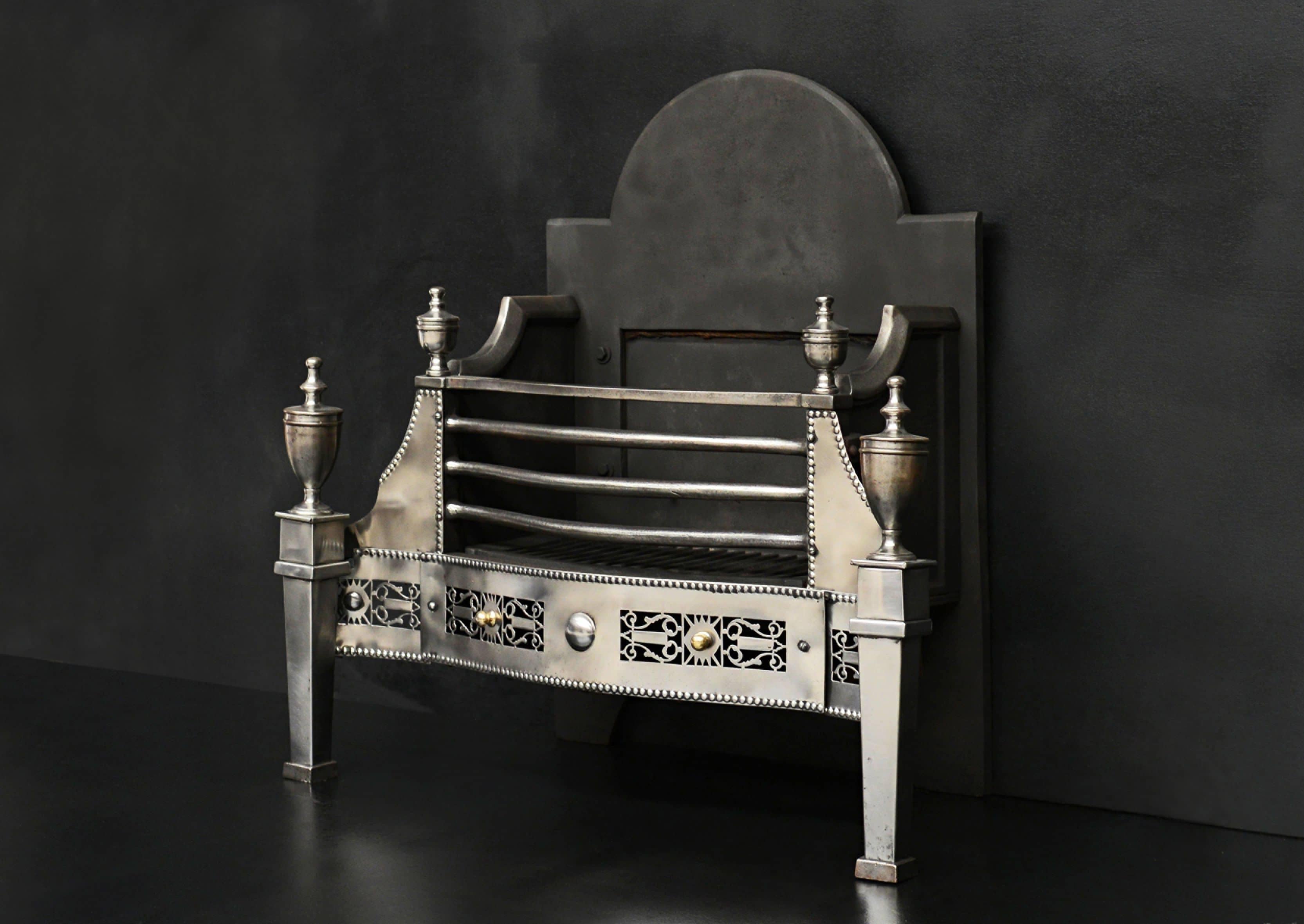 A polished steel firegrate in the Georgian style. The pierced fret with lyre motifs throughout and small brass balls. The tapering feet surmounted by classical urns. Bowed front bars with urns above. English, circa 1900. 

Width At Front: 765 mm