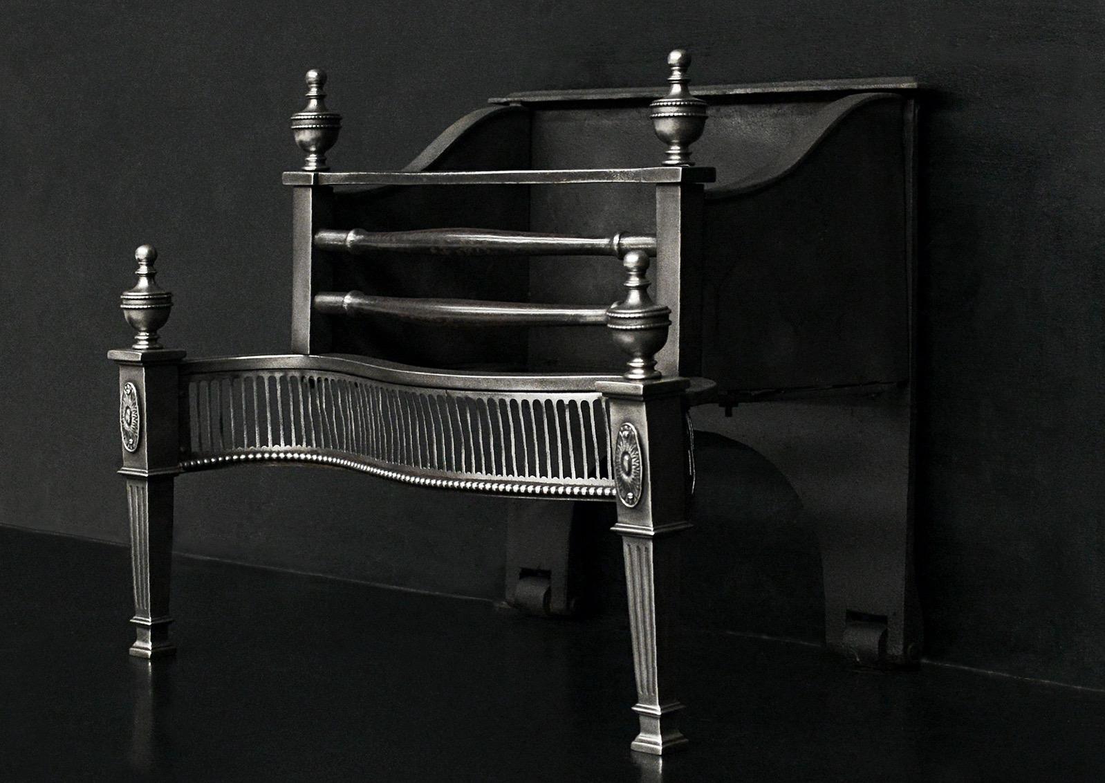 A polished steel Georgian style firegrate. The tapering legs with fluting and oval paterae, surmounted by urn finials with fine rope mouldings. The serpentine fret with fluting throughout and beading below. The burning area with shaped front bars