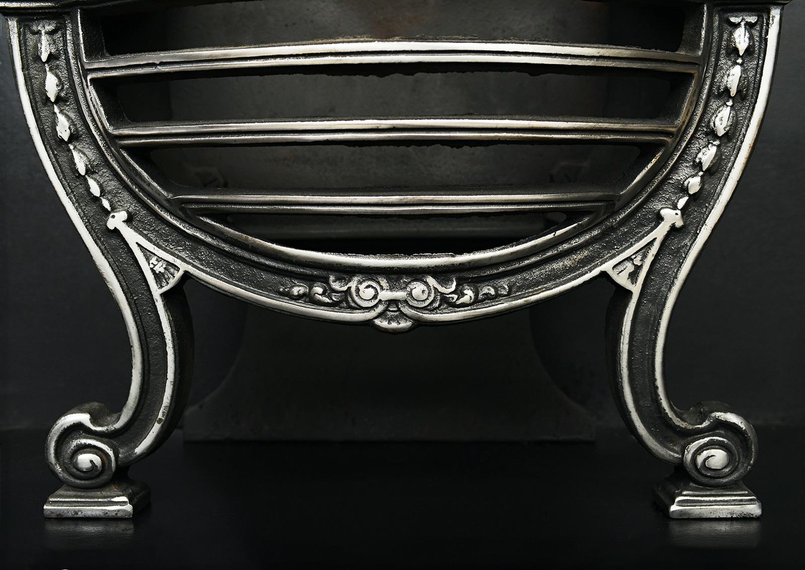 A polished wrought iron firegrate in the Adam style. The shaped feet surmounted by bowl shaped burning area with bowed front bars. Brass urn finials to top and decorative cast iron fireback behind. English, 20th century. 

Width At Front:	570 mm    