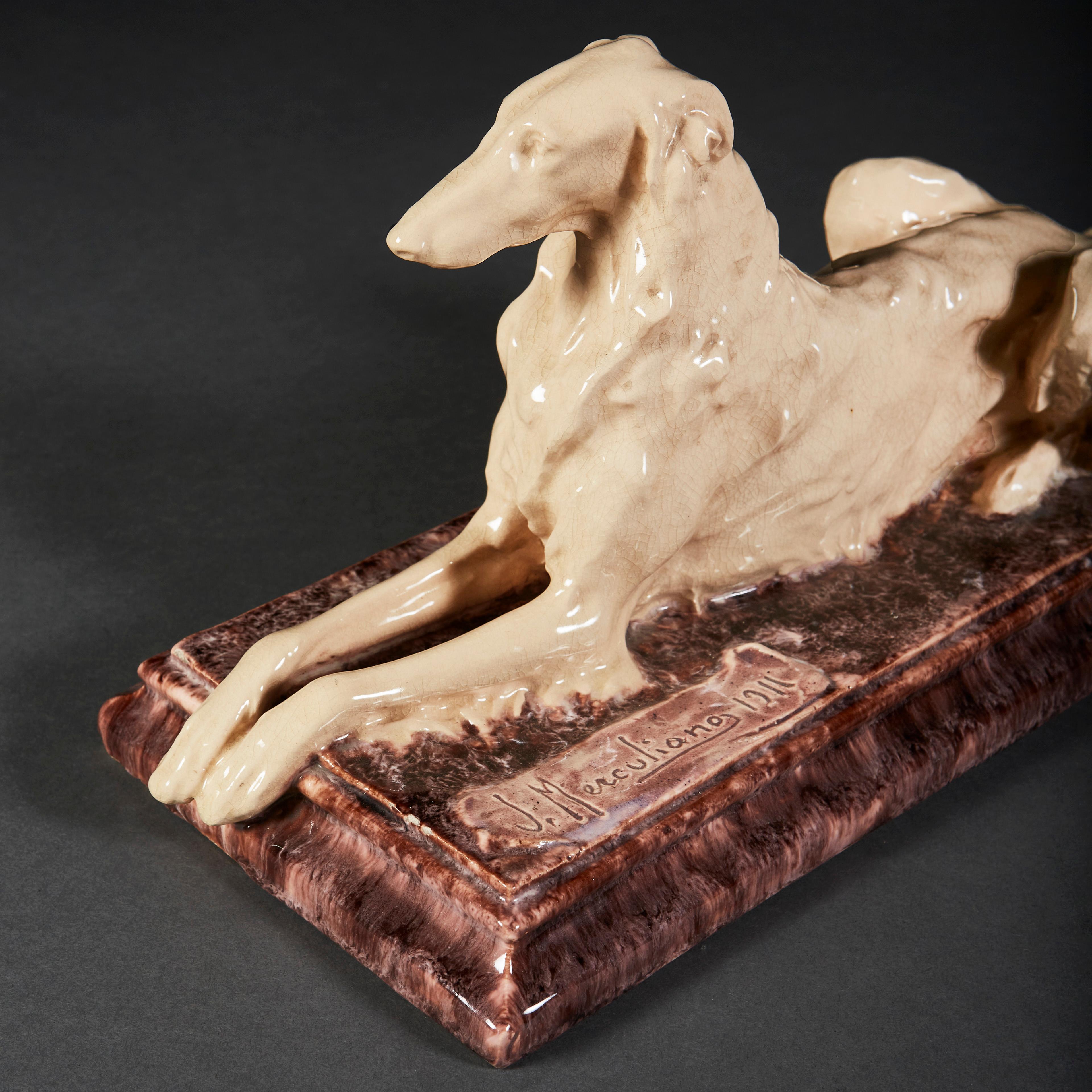 An unusual porcelain sculpture modeling a Borzoi dog in recumbent position, the body in white porcelain glaze, the base with marbleized red glaze. Signed J Merculiano, 1911.