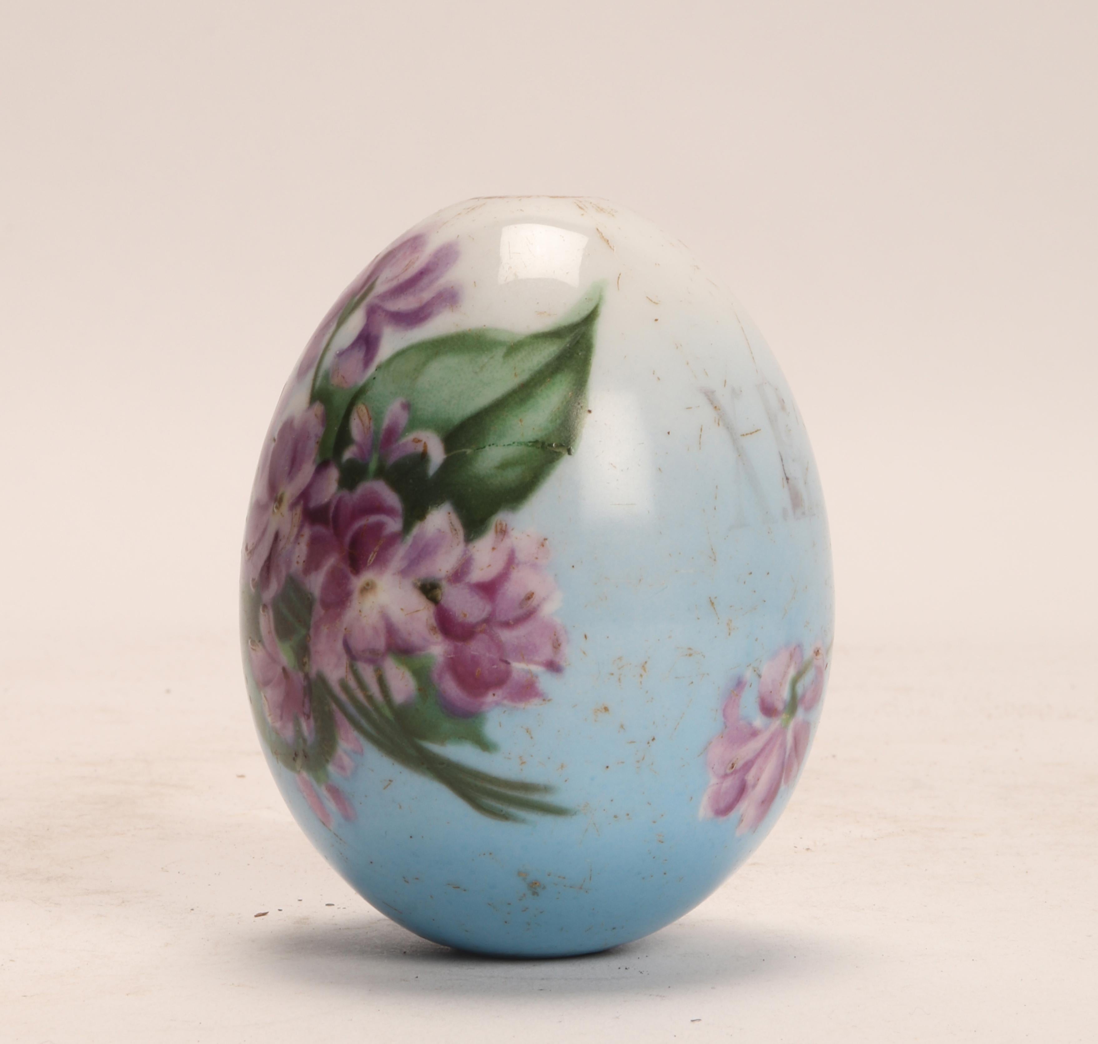 A painted porcelain Easter egg, depicting a bunch of violet flowers on one side, while on the other side the cyrillic monogram: C.R. (Risen Christ), on a blue background. Russia, circa 1890.