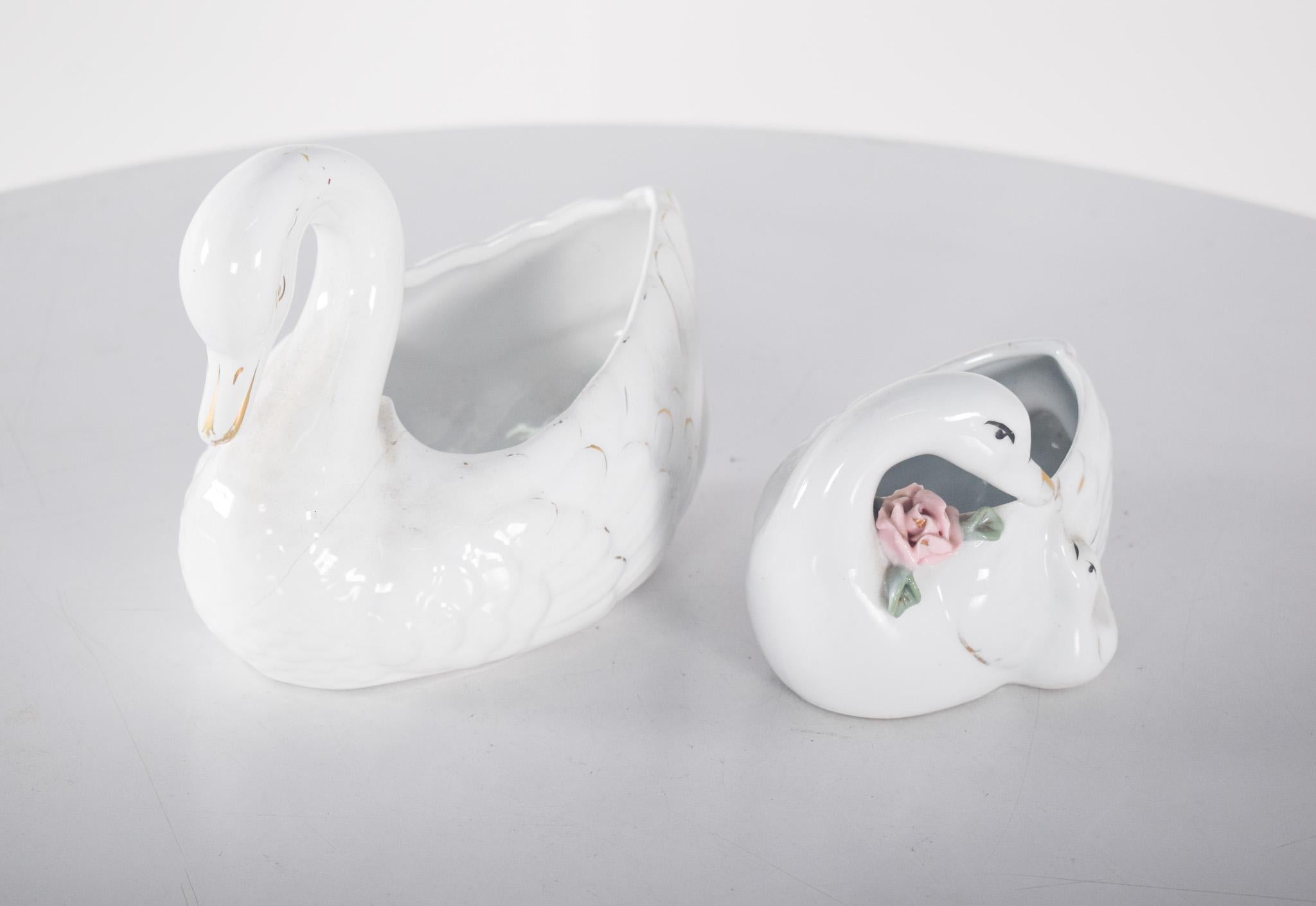 Un cigno in ceramica portoghese e un'anatra in ceramica cinese. Il cigno, più grande e imponente, ha un corpo scolpito con delicati dettagli sulle piume che ne sottolineano l'aspetto elegante. È di colore bianco con tocchi d'oro sul becco e sulle