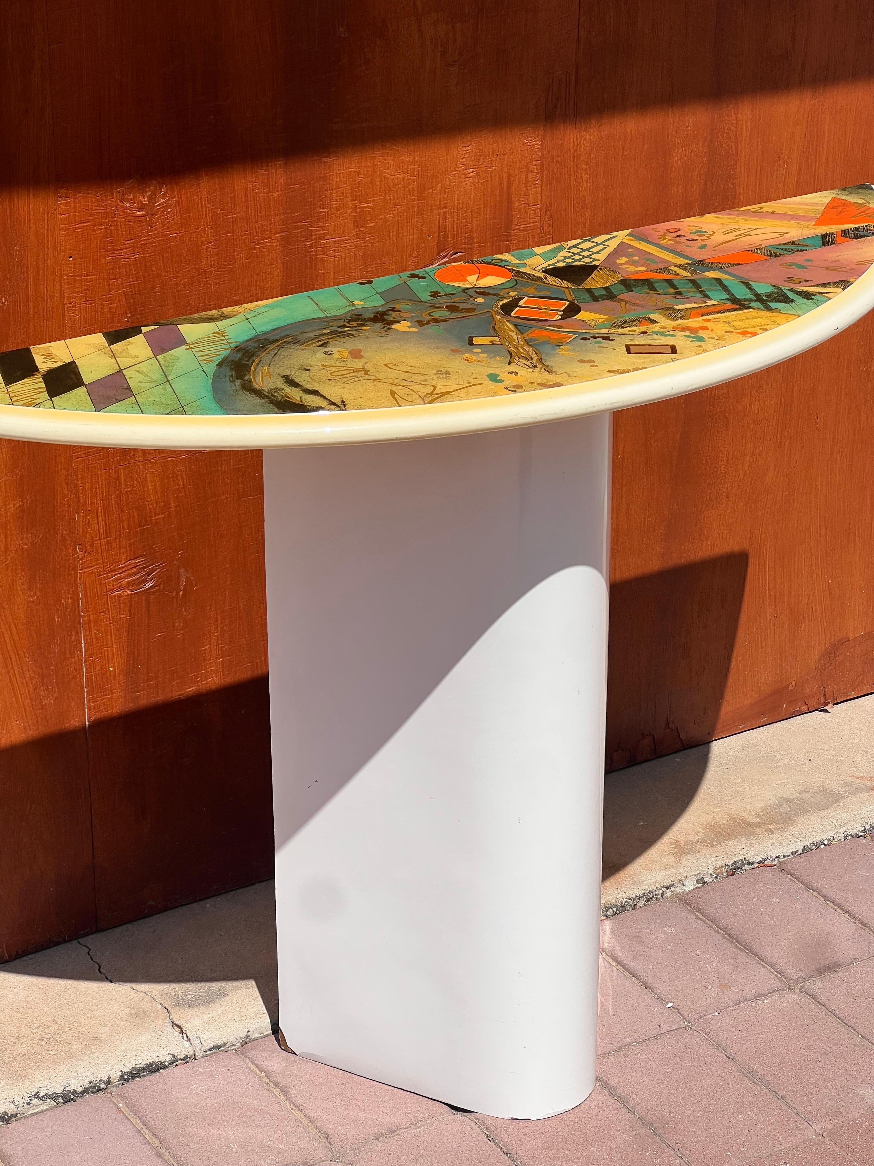 A striking and very unique matching set including a Demi-lune console and eye-shaped mirror with colorful postmodern motif, circa 1980. Each piece is lacquered wood, and the mirror is ready to hang.