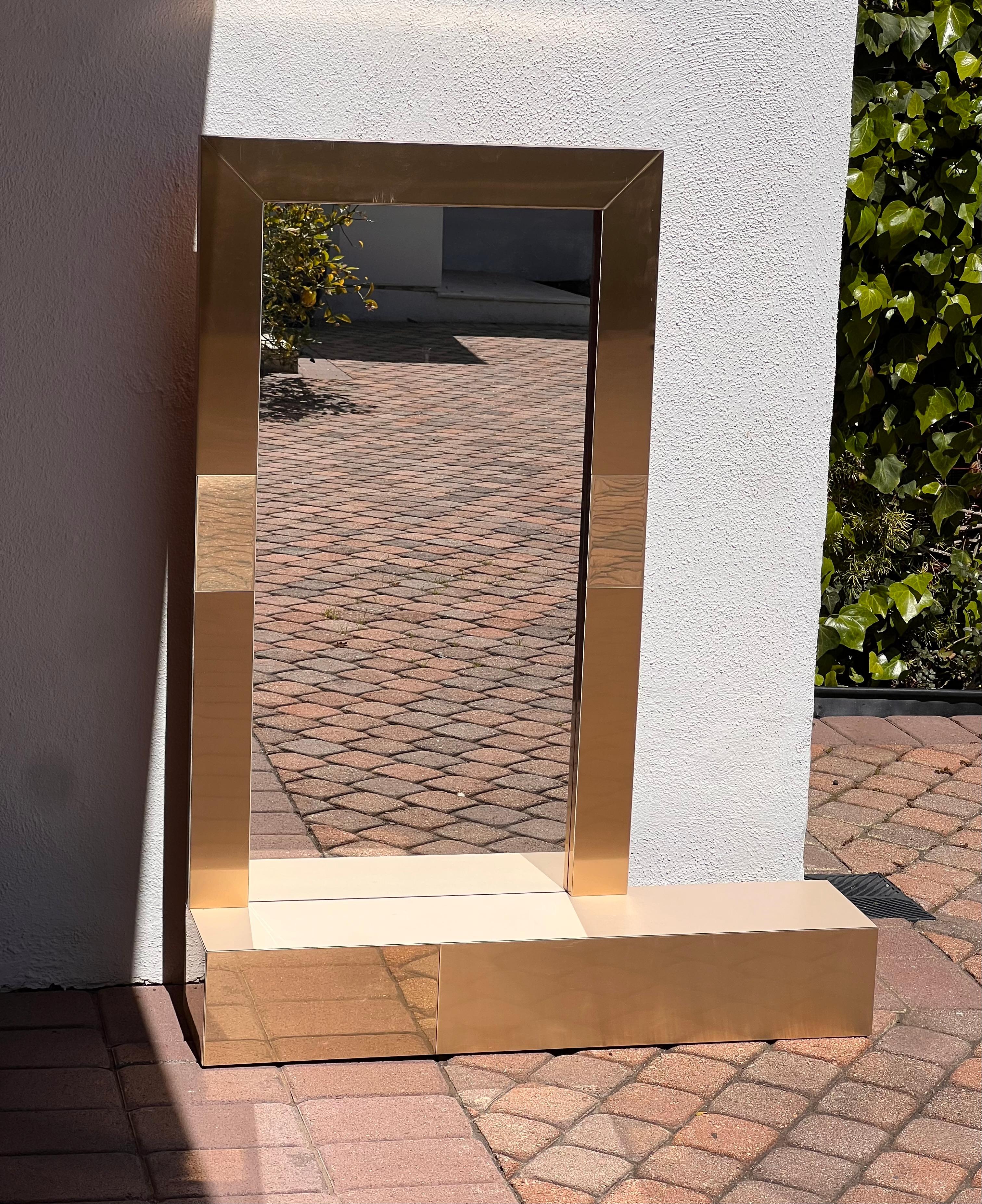 A postmodern Paul Evans style wall-mount vanity mirror with shelf, circa late 1970s or early 1980s. The gorgeous blend of metallics in this piece will add sophisticated glamour to any interior. 
36” W x 8.5” D x 46.4” H 
Mirror portion is 24” W x