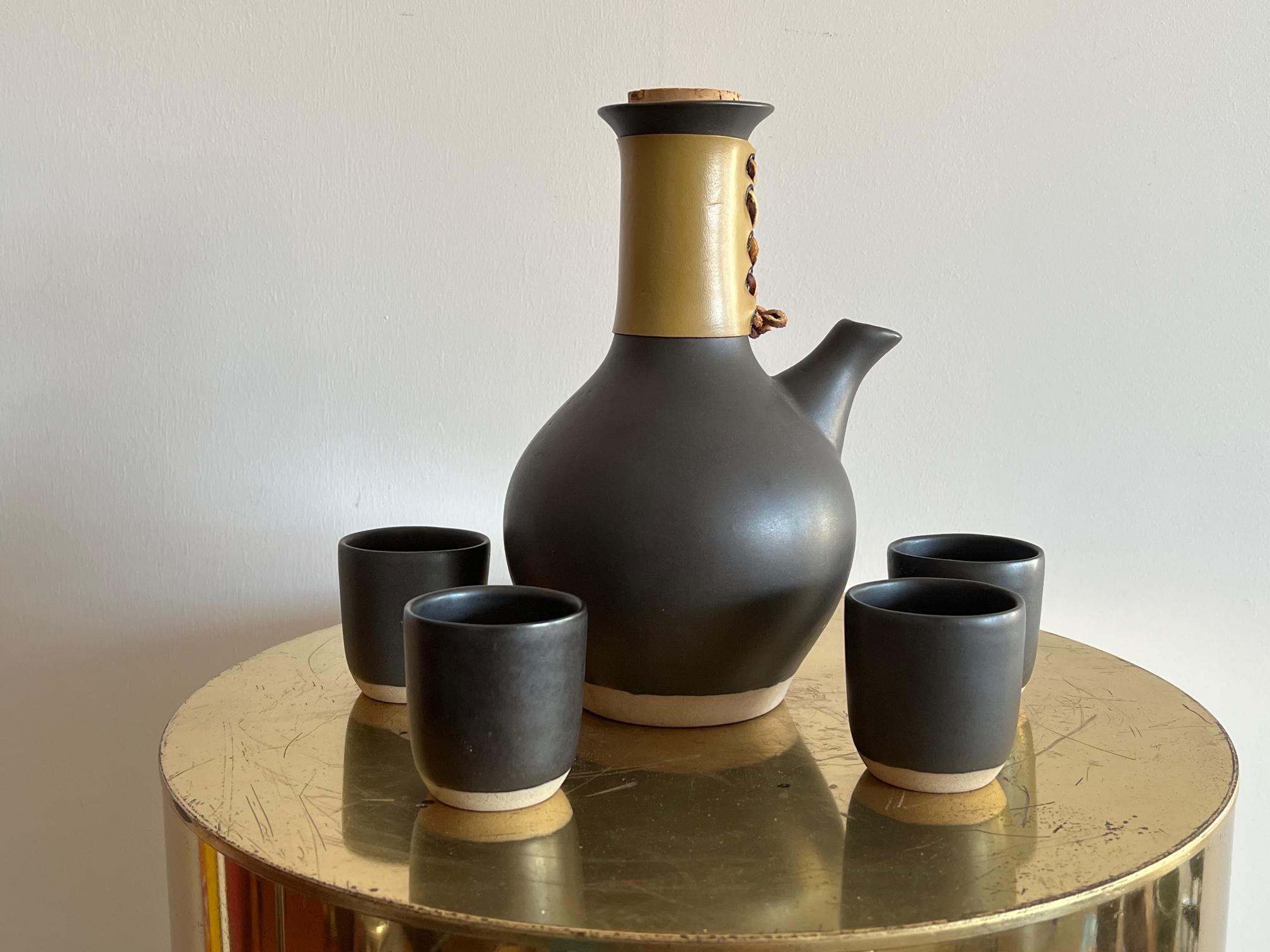 An elegant coffee or tea set by Marshall Studios/Martz consisting of a large coffee pot with leather holder and four matching cups. Beautiful dark brown/almost black glaze, handmade. Measures: The pot is approx. 10