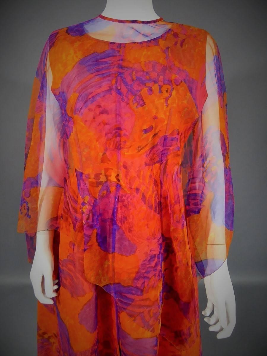 Début 1970 en France.
Robe longue sans manches de Haute Couture de Madame Grès. Bas de la robe orange sur laquelle est cousue une mousseline imprimée de grandes fleurs abstraites orange et violettes. Intérieur structuré à la taille. Forme de la jupe